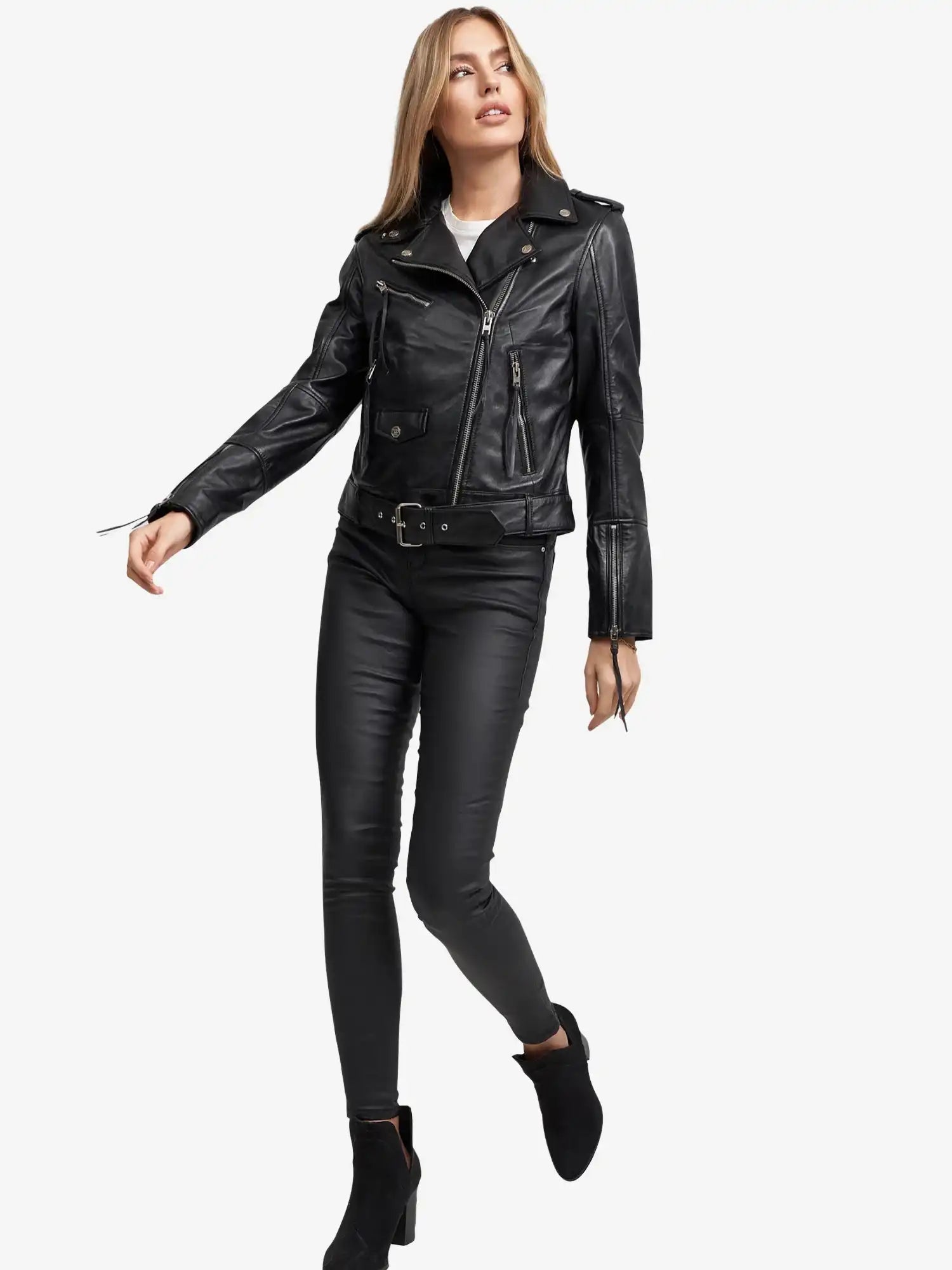 Eine Frau trägt die Milena Lederjacke mit Gürtel von trueprodigy mit schwarzer, taillierter Hose und Stiefeletten und steht vor einem weißen Hintergrund. Sie hat lange blonde Haare, blickt zur Seite und streckt einen Arm aus.