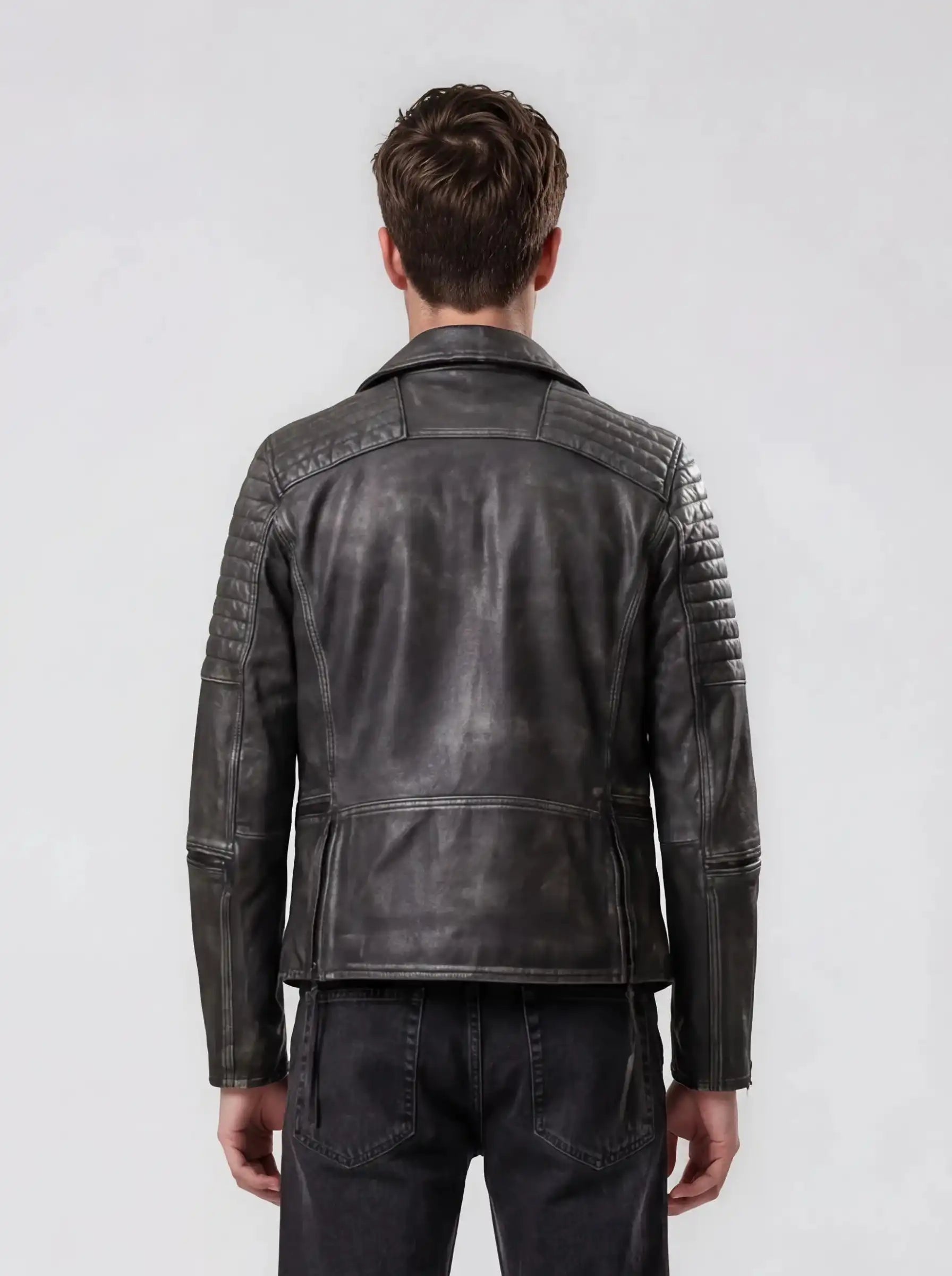 Eine Person mit kurzen braunen Haaren wird von hinten gezeigt. Sie trägt die trueprodigy Vintage Biker Lederjacke Herren "Bryan" mit Steppung und verblasste schwarze Jeans vor einem schlichten hellen Hintergrund.