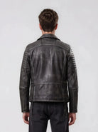 Eine Person mit kurzen braunen Haaren wird von hinten gezeigt. Sie trägt die trueprodigy Vintage Biker Lederjacke Herren "Bryan" mit Steppung und verblasste schwarze Jeans vor einem schlichten hellen Hintergrund.