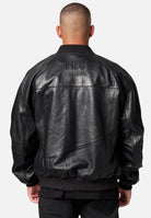 Eine Person steht mit dem Rücken zur Kamera und trägt eine trueprodigy Filip Oversized Bomber-Lederjacke mit dem großen TRUE PRODIGY-Schriftzug auf dem Rücken. Der Hintergrund ist hell und schlicht.