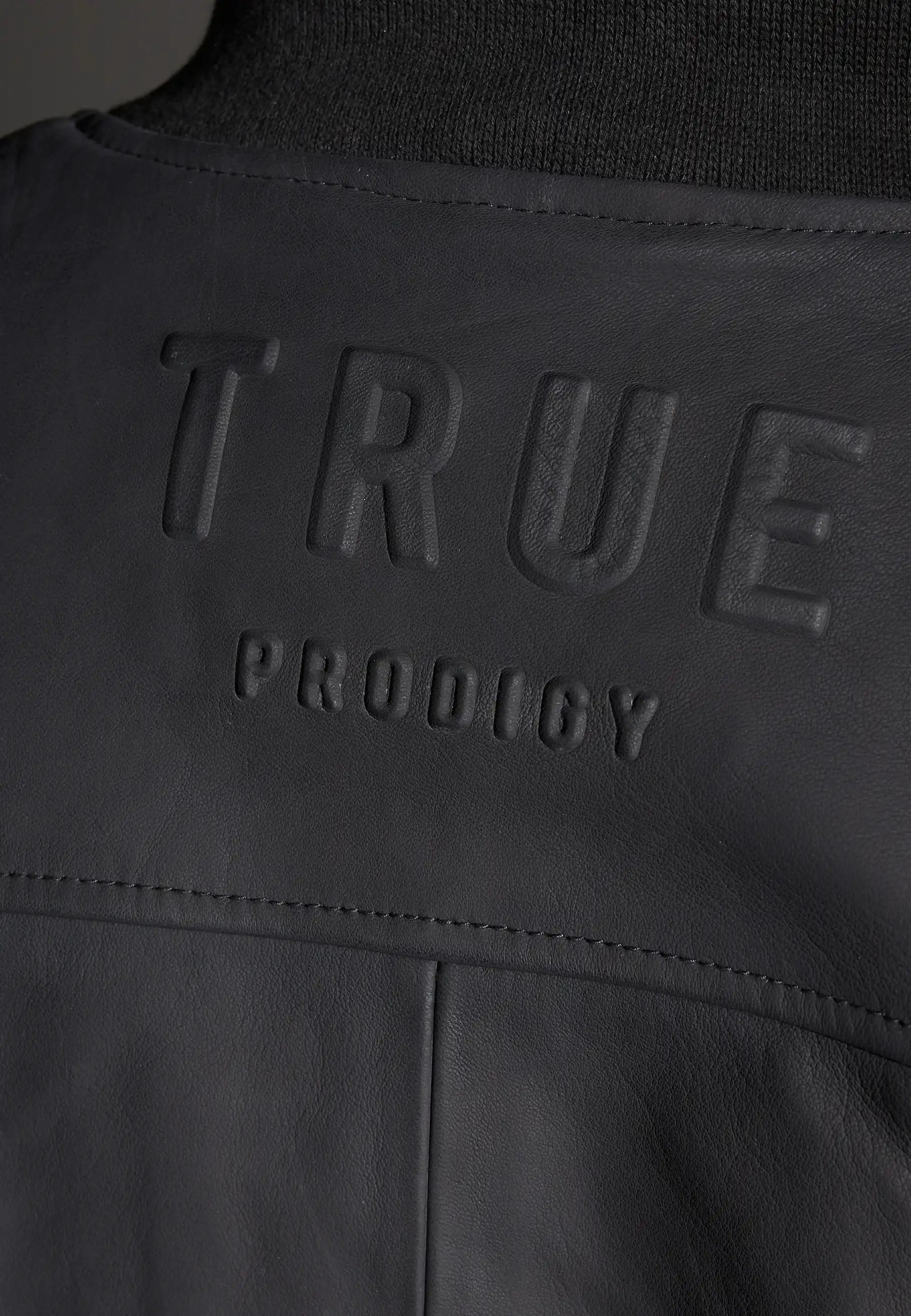 Nahaufnahme einer schwarzen Nazar Oversized Bomber-Lederjacke matt von trueprodigy mit großem, erhabenem trueprodigy-Schriftzug, der quer über den Rücken geprägt ist.