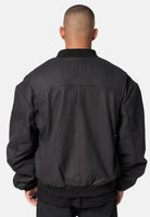 Eine Person mit kurzen Haaren, von hinten gesehen, trägt eine schwarze Nazar Oversized Bomber-Lederjacke matt von trueprodigy. Auf dem oberen Rücken ist "trueprodigy" vor einem schlichten hellen Hintergrund eingeprägt.