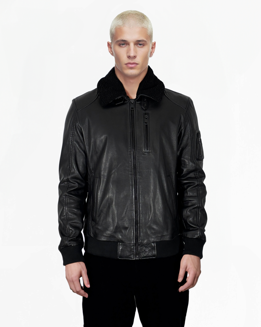 Eine Person mit kurzen blonden Haaren trägt die Blaze-Jacke von trueprodigy aus schwarzem Schafsleder. Sie hat einen Reißverschluss vorne und einen strukturierten Kragen. Die Hände sind lässig in den Reißverschlusstaschen vor einem schlichten weißen Hintergrund verstaut.