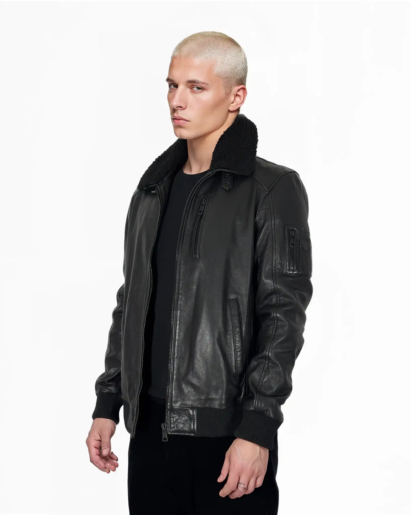 Eine Person mit kurzen, gebleichten blonden Haaren trägt die trueprodigy Blaze Moderne Fliegerjacke aus echtem Leder mit abnehmbarem Teddy-Kragen und ein schwarzes Hemd und steht mit neutralem Gesichtsausdruck vor einem schlichten weißen Hintergrund.