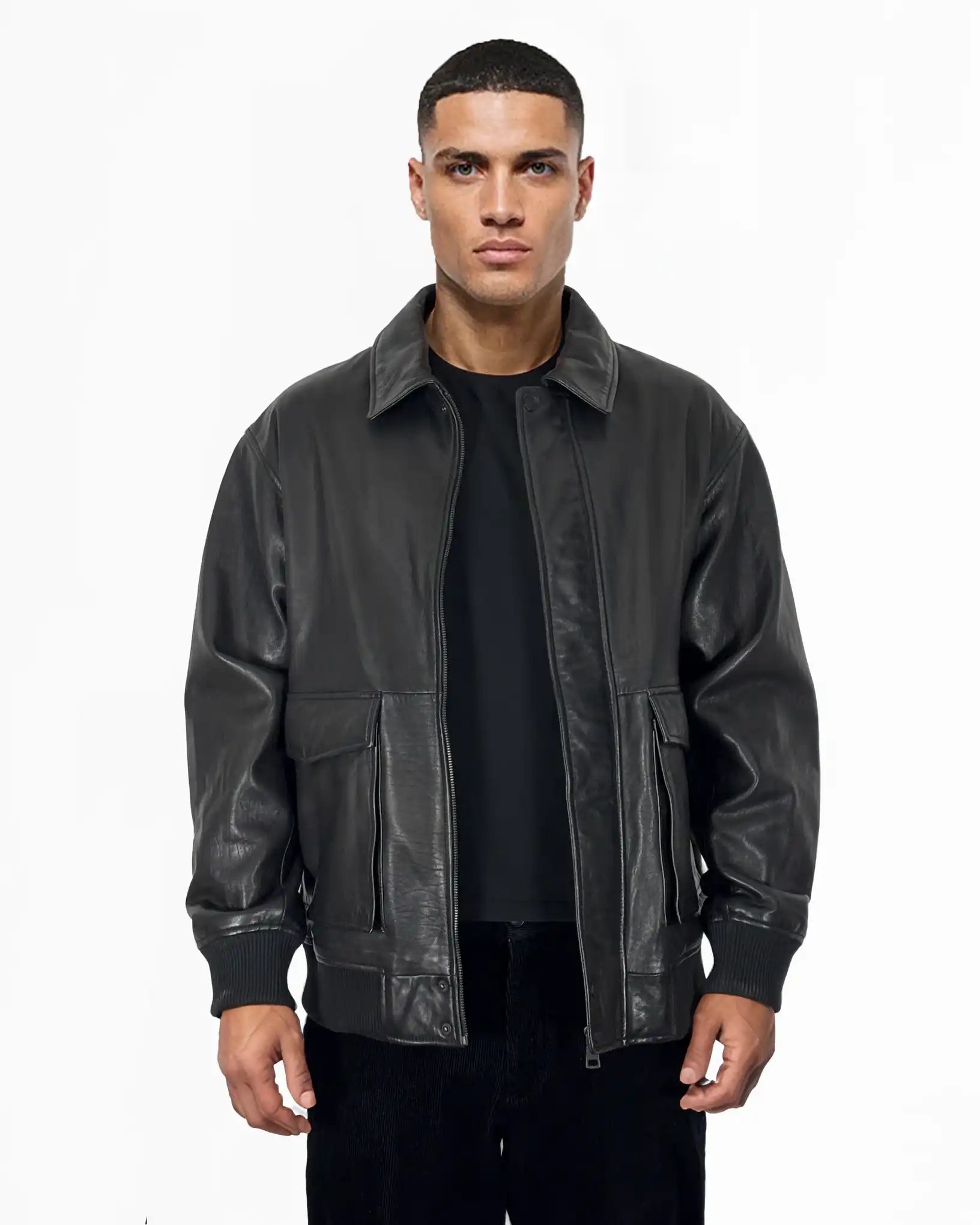 Ein Mann blickt nach vorne, er trägt eine Trueprodigy Ryder Oversize-Lederjacke mit Stehkragen, 3D-Silikonlogo & Retro-Details über einem schwarzen Hemd und einer Hose, vor einem schlichten weißen Hintergrund.