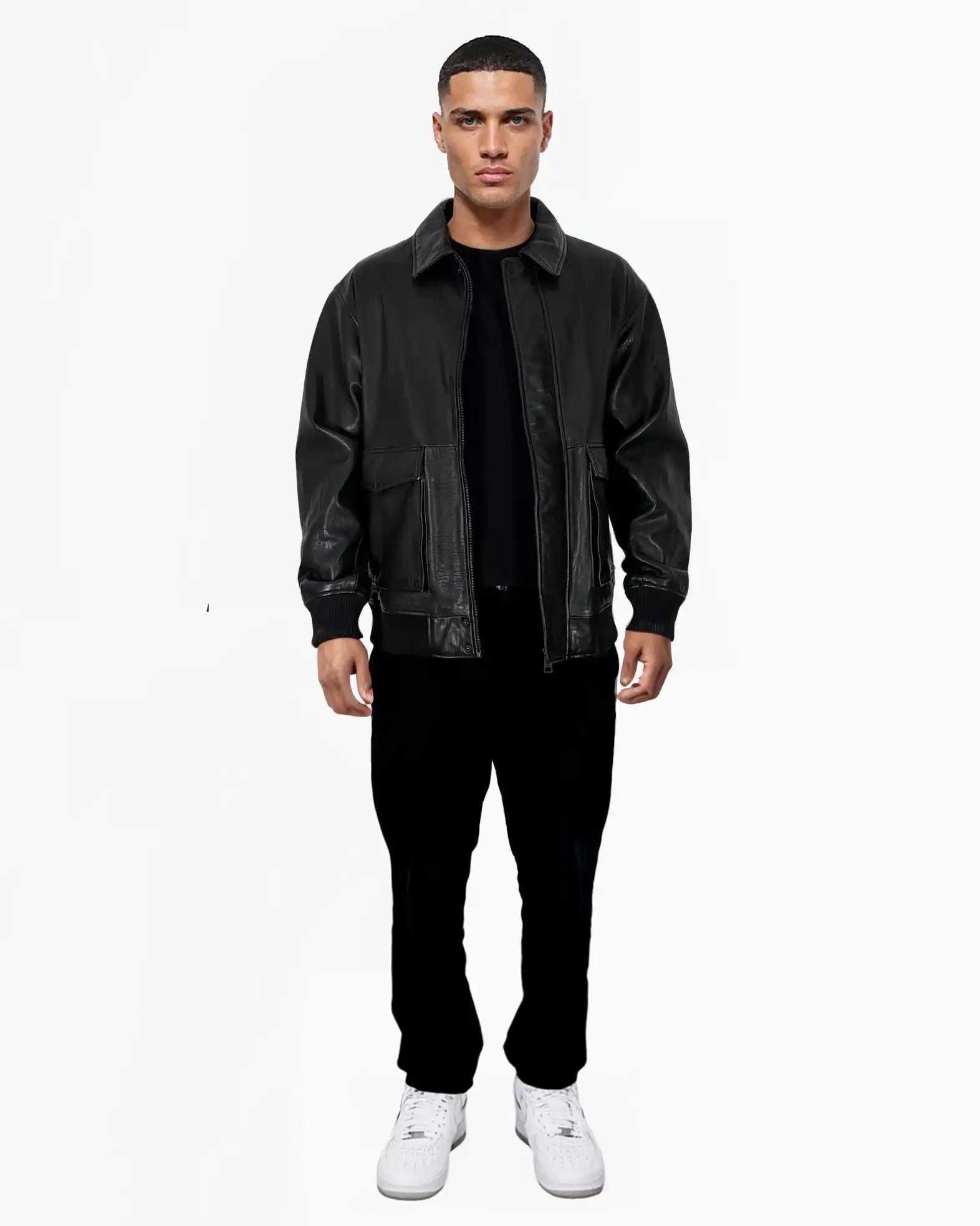 Ein Mann steht vor einem weißen Hintergrund und trägt die Ryder Oversize-Lederjacke mit Stehkragen, 3D-Silikonlogo & Retro-Details von trueprodigy, gepaart mit einer schwarzen Hose, einem schwarzen Hemd und weißen Turnschuhen. Seine Arme ruhen an den Seiten.