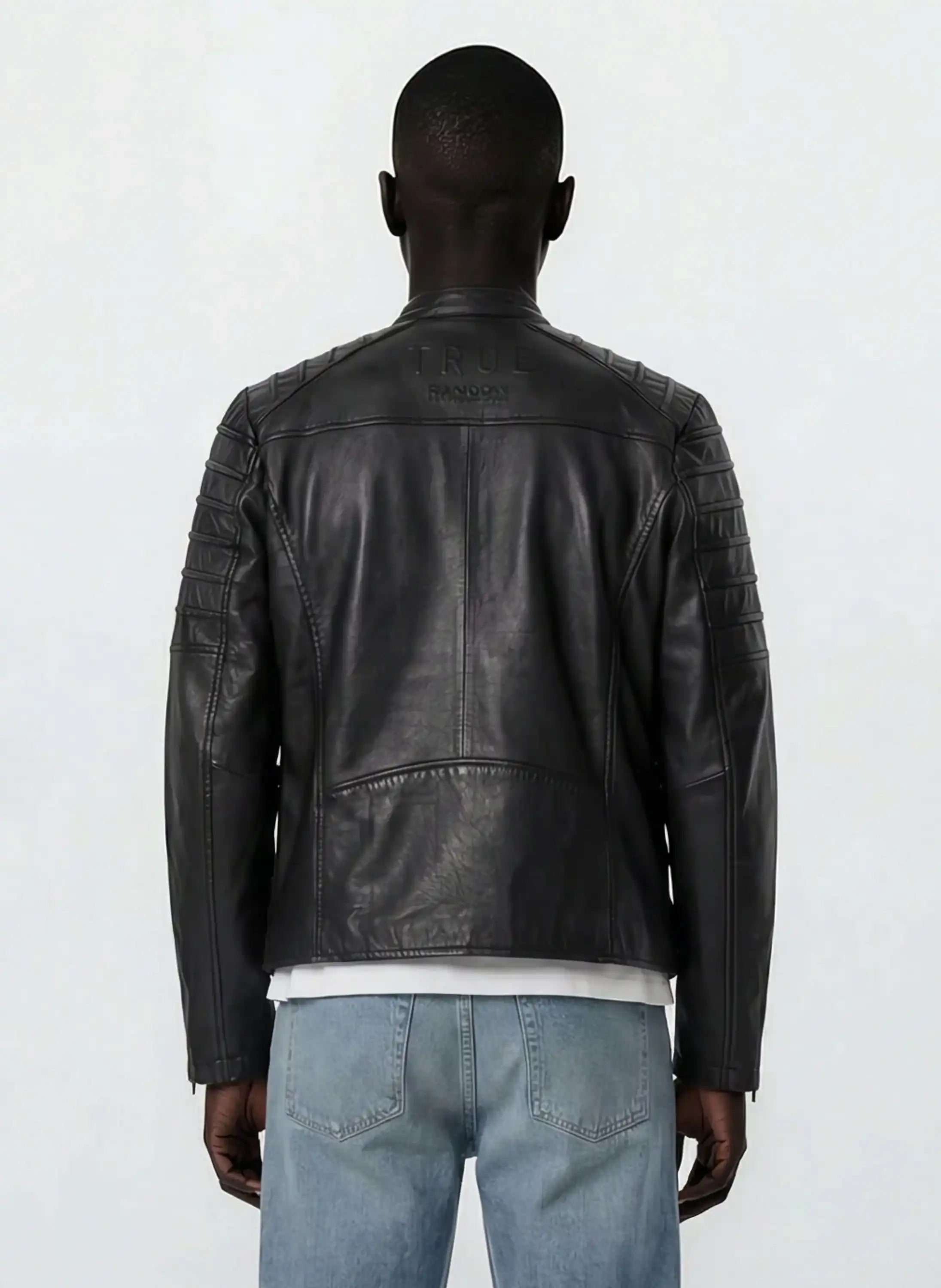 Eine Person steht mit dem Rücken zur Kamera und trägt eine schwarze trueprodigy Slim-Fit-Lederjacke mit Stehkragen & Zipper-Details mit abgesteppten Schultern und hellblauen Jeans. TRUE und TRANOLOGY sind in der Nähe des Kragens auf dem Rücken eingeprägt.