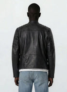 Eine Person steht mit dem Rücken zur Kamera und trägt eine schwarze trueprodigy Slim-Fit-Lederjacke mit Stehkragen & Zipper-Details mit abgesteppten Schultern und hellblauen Jeans. TRUE und TRANOLOGY sind in der Nähe des Kragens auf dem Rücken eingeprägt.