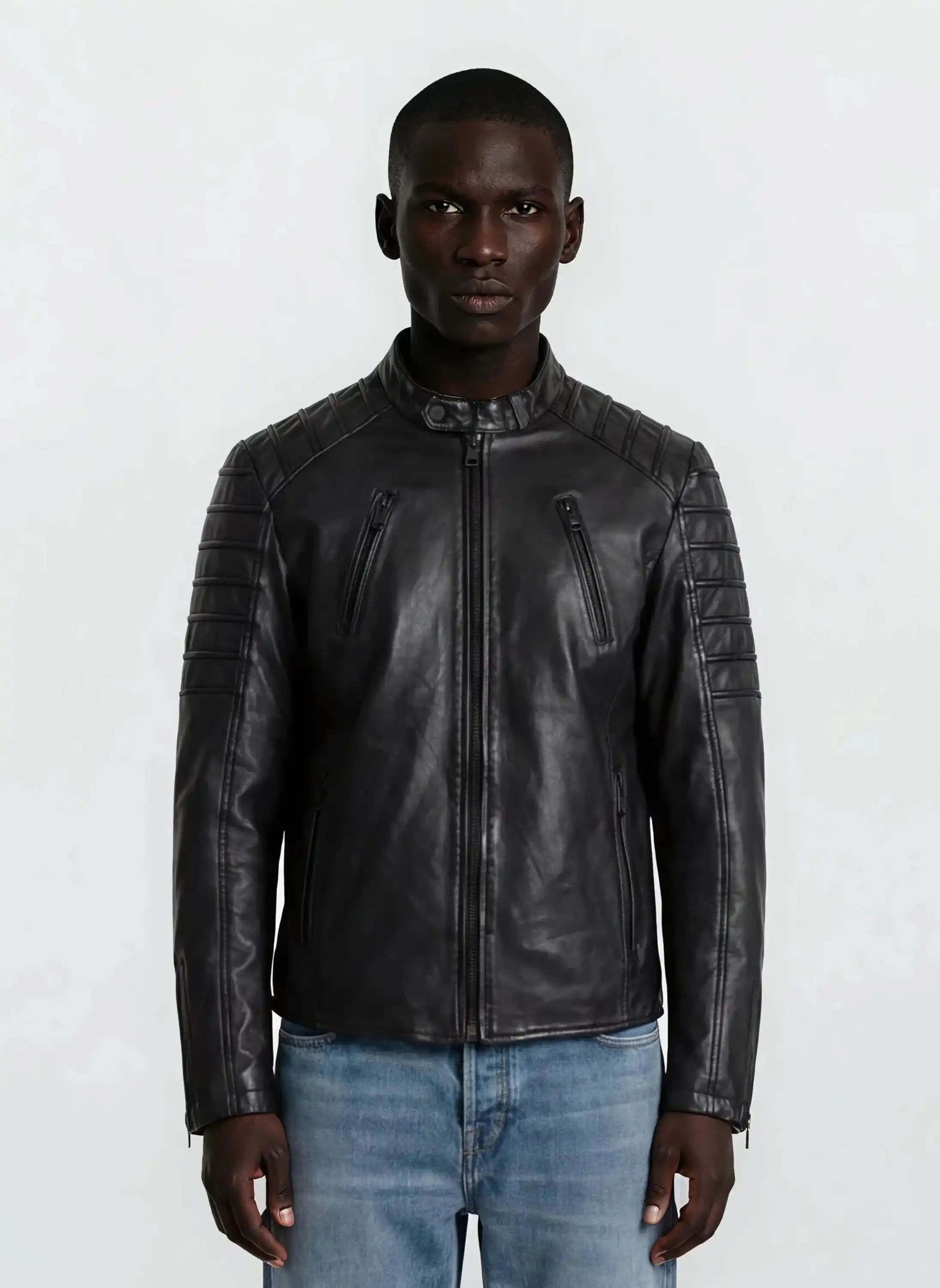 Eine Person blickt nach vorne in einer trueprodigy Slim-Fit-Lederjacke mit Stehkragen & Zipper-Details, mit gesteppten Schultern und Ärmeln, gepaart mit hellblauen Jeans vor einem schlichten hellen Hintergrund.