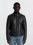Eine Person blickt nach vorne in einer trueprodigy Slim-Fit-Lederjacke mit Stehkragen & Zipper-Details, mit gesteppten Schultern und Ärmeln, gepaart mit hellblauen Jeans vor einem schlichten hellen Hintergrund.