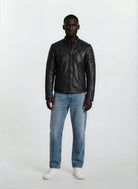 Eine Person steht mit dem Gesicht nach vorne vor einem schlichten weißen Hintergrund und trägt eine trueprodigy Slim-Fit-Lederjacke mit Stehkragen & Zipper-Details, hellblaue Jeans und weiße Turnschuhe.