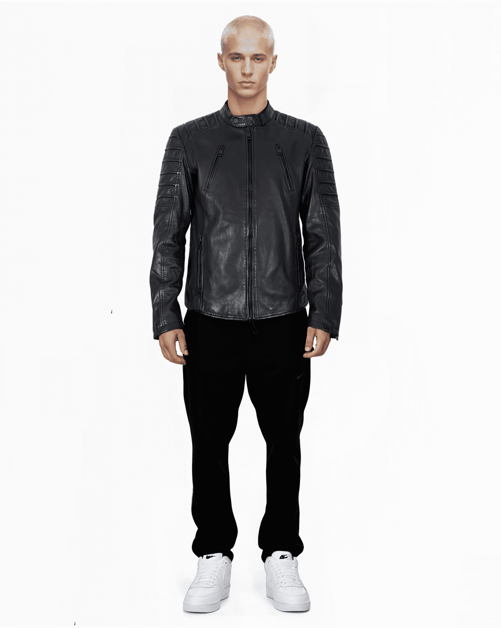 Eine Person mit kurzen, hellen Haaren steht vor einem weißen Hintergrund. Sie trägt Dash – eine elegante schwarze Lederjacke von trueprodigy mit Stehkragen. Dazu eine schwarze Hose und weiße Turnschuhe. Die Hände hängen an den Seiten und der Blick ist direkt in die Kamera gerichtet.