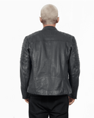 Eine Person mit kurzen, hellen Haaren ist von hinten zu sehen. Sie trägt eine schwarze Trueprodigy Dash-Jacke mit gesteppten Schulterdetails und dem Schriftzug „TRUE“ oben. Die Jacke hat einen eleganten Stehkragen, der perfekt zur dunklen Hose passt.