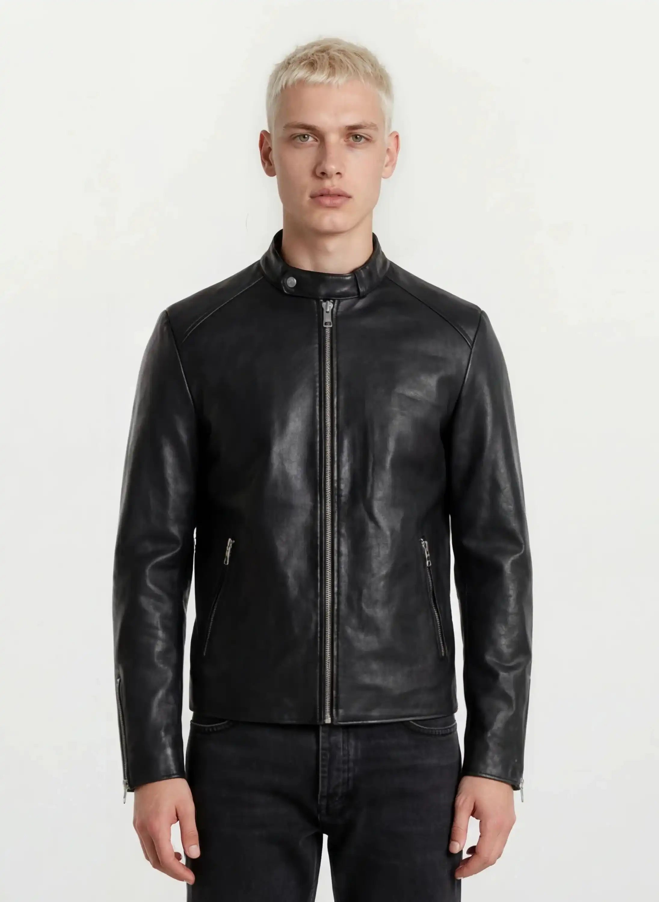 Eine Person mit kurzen blonden Haaren trägt die trueprodigy Slim-Fit-Lederjacke mit sichtbarem 3D-Rückenlogo und schwarze Jeans, steht vor einem schlichten weißen Hintergrund und blickt in die Kamera.