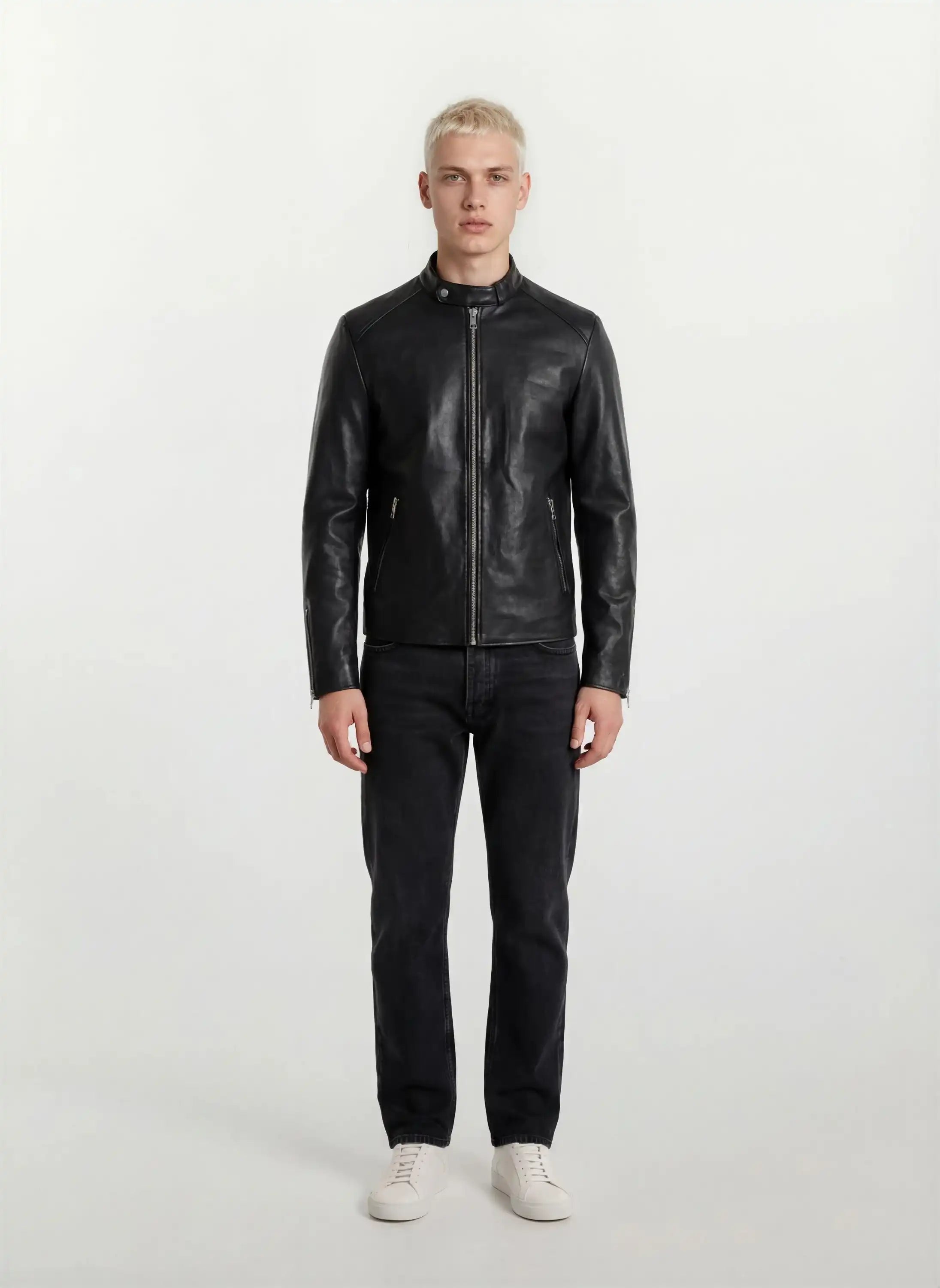 Eine Person mit kurzen blonden Haaren steht mit dem Gesicht nach vorne und trägt eine trueprodigy Slim-Fit-Lederjacke mit sichtbarem 3D-Rückenlogo, dunkle Jeans und weiße Turnschuhe vor einem schlichten weißen Hintergrund.