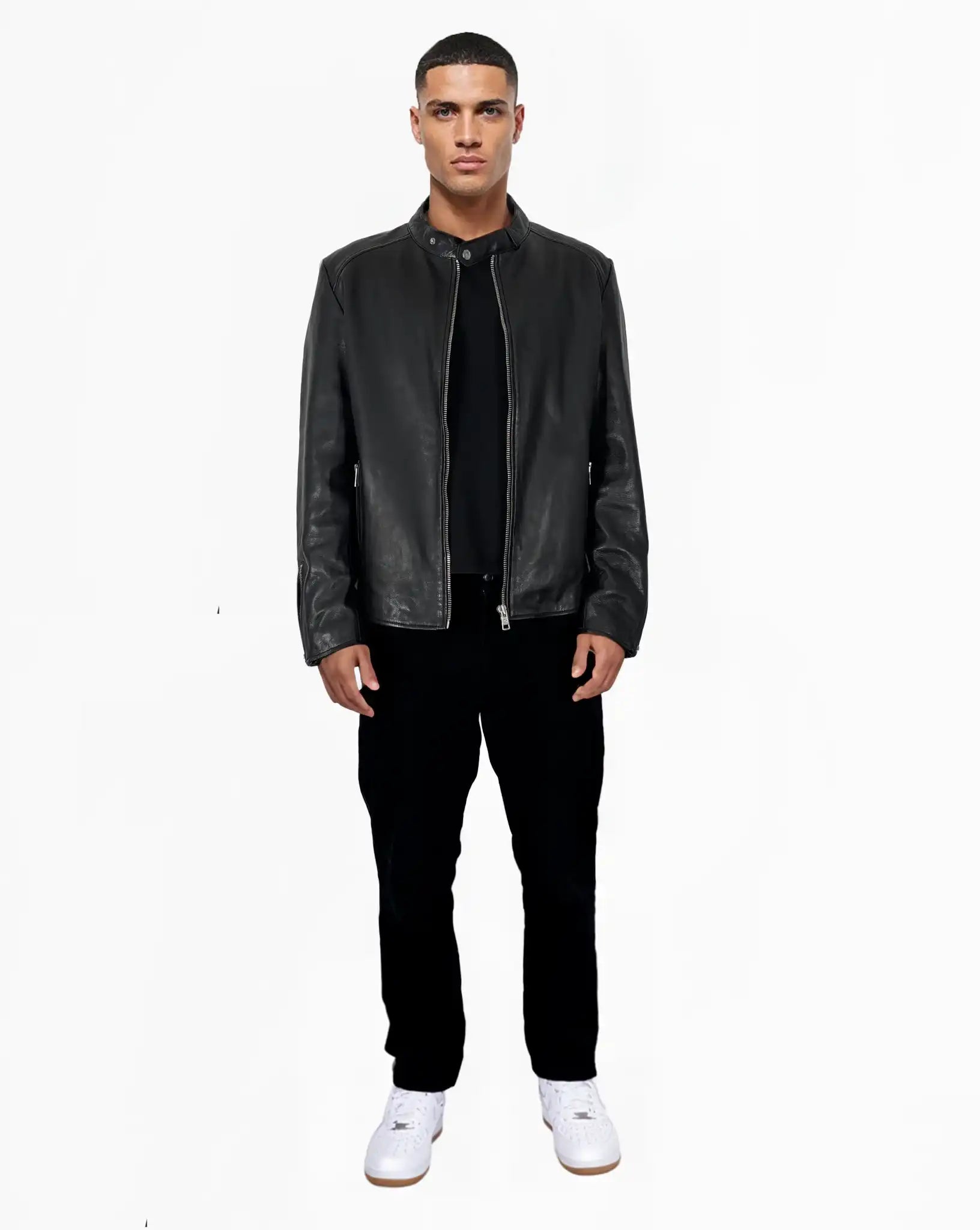 Ein Mann steht mit dem Gesicht nach vorne vor einem schlichten weißen Hintergrund und trägt die trueprodigy Jonas Slim-Fit-Lederjacke mit sichtbarem 3D-Rückenlogo, gepaart mit einem schwarzen Hemd, einer schwarzen Hose und weißen Sneakers.