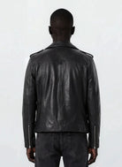 Eine Person mit kurzen Haaren trägt eine trueprodigy Leder-Bikerjacke mit asymmetrischem Zipper & 3D-Logo unter dem Kragen und schwarze Jeans, steht mit dem Rücken zur Kamera und präsentiert einen coolen Biker-Look vor einem schlichten hellen Hintergrund.