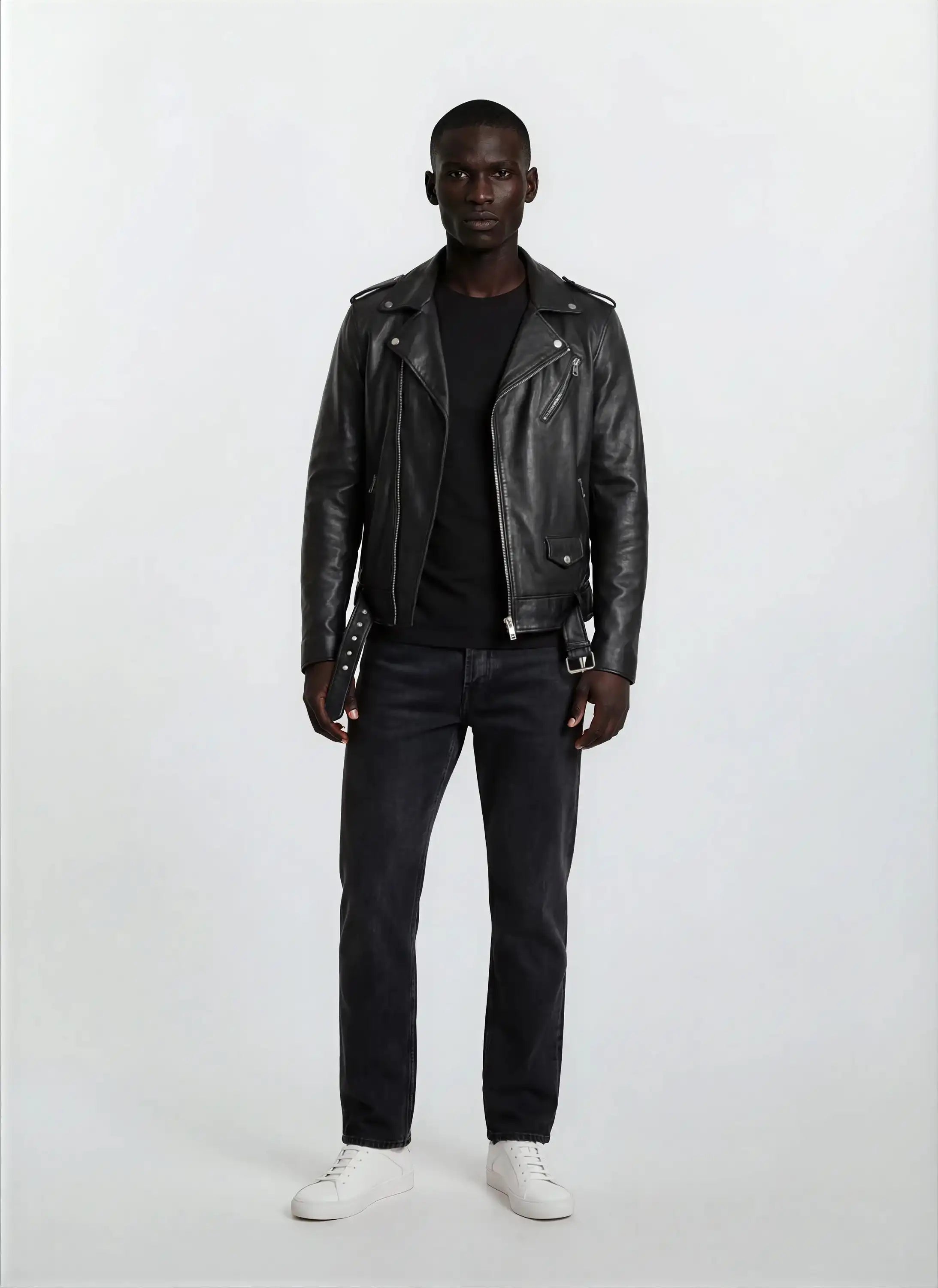 Eine Person blickt vor einem weißen Hintergrund nach vorne und trägt die Leder-Bikerjacke mit asymmetrischem Zipper & 3D-Logo unter dem Kragen von trueprodigy, gestylt mit einem schwarzen T-Shirt, dunklen Jeans und weißen Sneakers für einen Biker-Look.