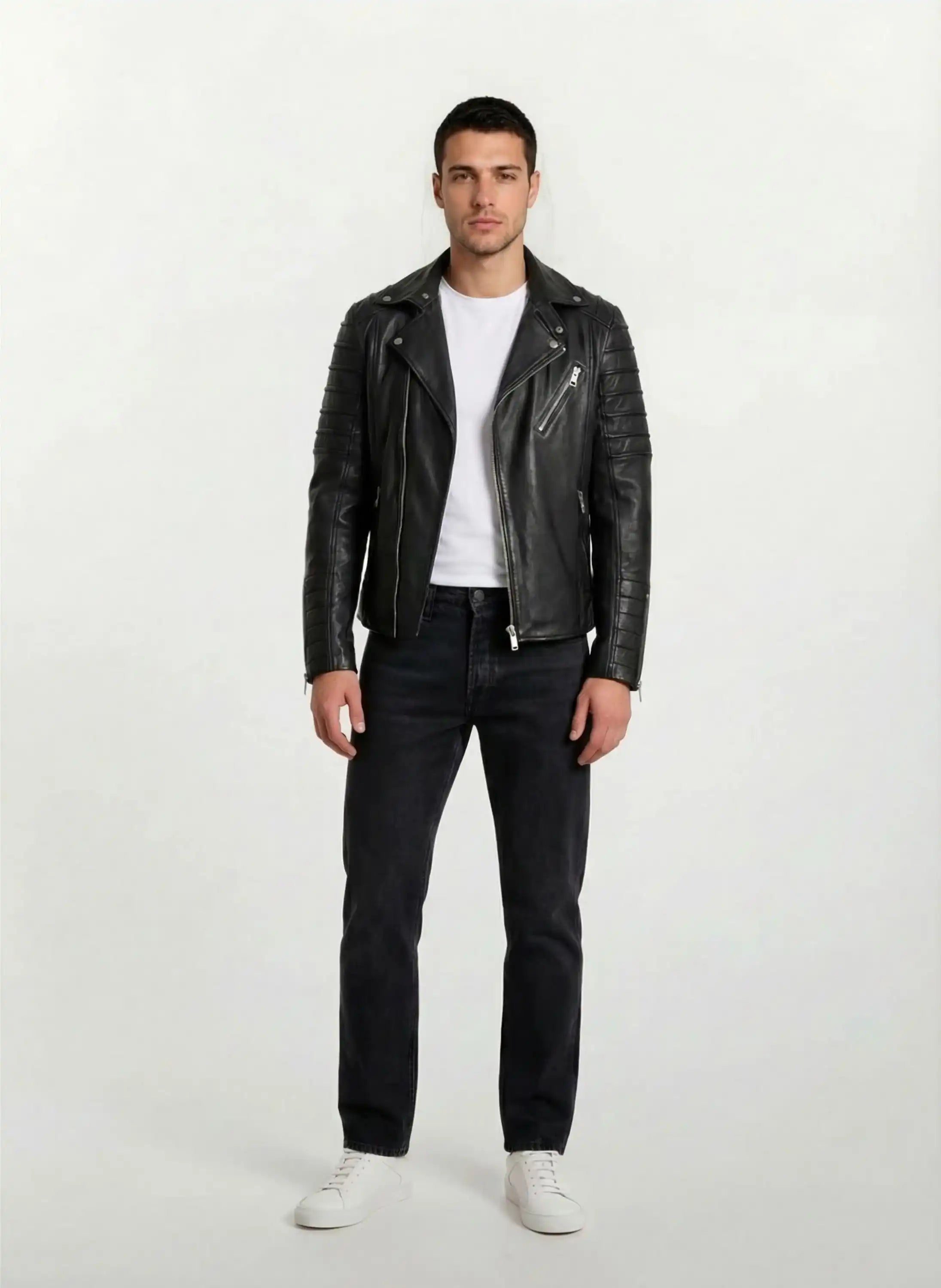 Ein Mann blickt nach vorne und trägt die trueprodigy Lederjacke mit Paspelierung und diversen Reißverschlüssen über einem weißen T-Shirt, dazu dunkle Jeans und weiße Turnschuhe. Der Hintergrund ist einfarbig und hell.