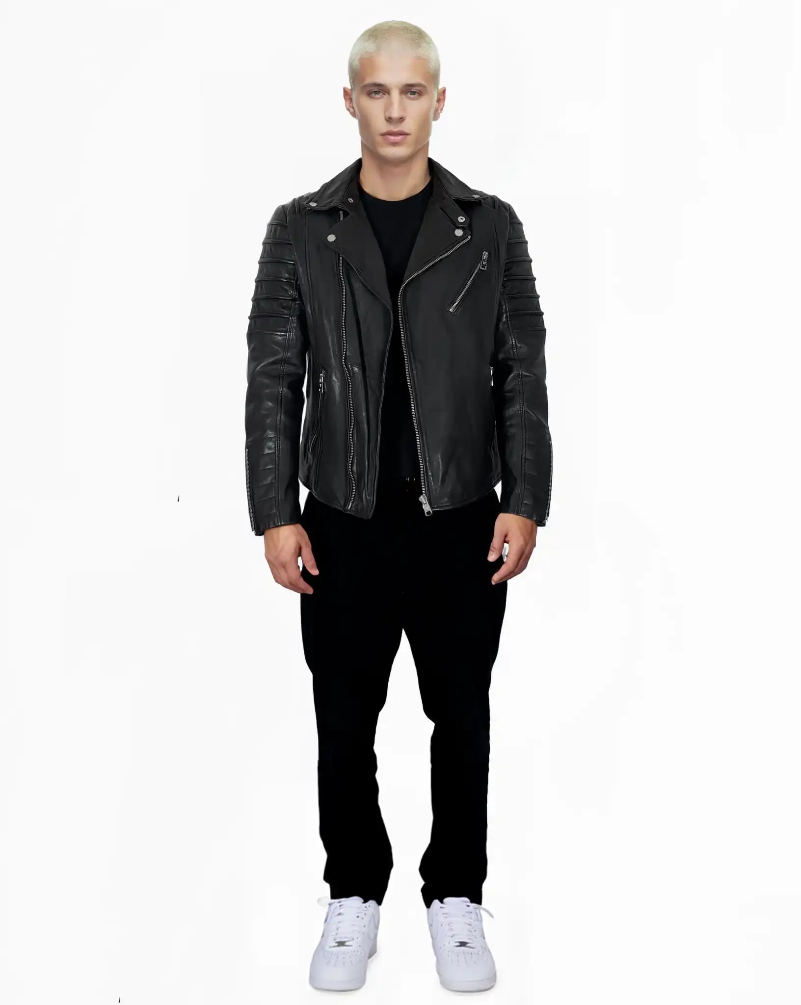 Eine Person mit kurzen blonden Haaren steht vor einem weißen Hintergrund und trägt die John schwarze Schafsleder Jacke von trueprodigy, zusammen mit einer schwarzen Hose, einem schwarzen Hemd und weißen Sneakers.