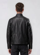 Von hinten sieht man einen Mann mit kurzen braunen Haaren, der eine schwarze Herren Lederjacke aus Schafsleder im klassischen Blouson-Schnitt von trueprodigy und schwarze Jeans vor hellem, schlichten Hintergrund trägt.