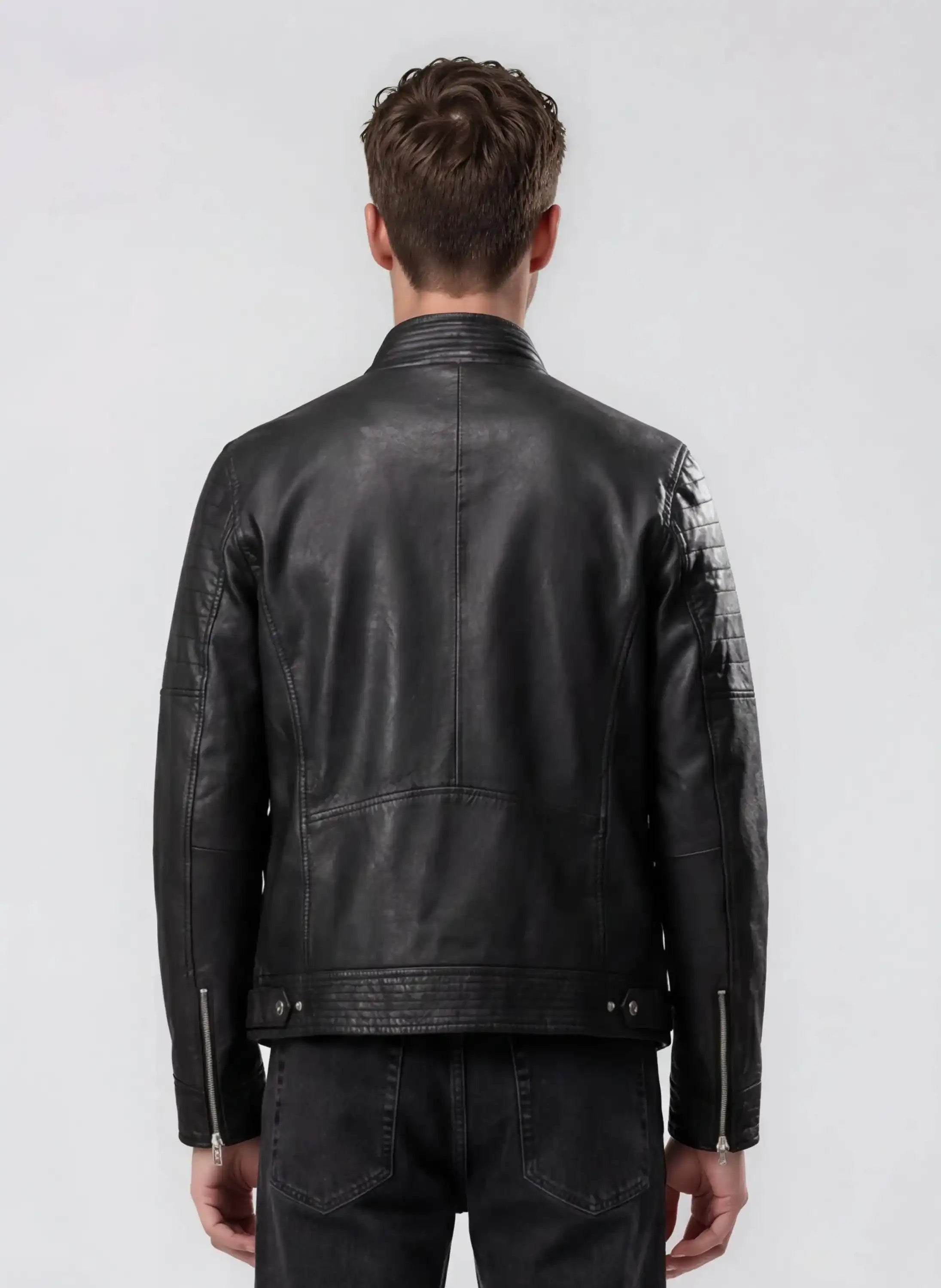 Von hinten sieht man einen Mann mit kurzen braunen Haaren, der eine schwarze Herren Lederjacke aus Schafsleder im klassischen Blouson-Schnitt von trueprodigy und schwarze Jeans vor hellem, schlichten Hintergrund trägt.