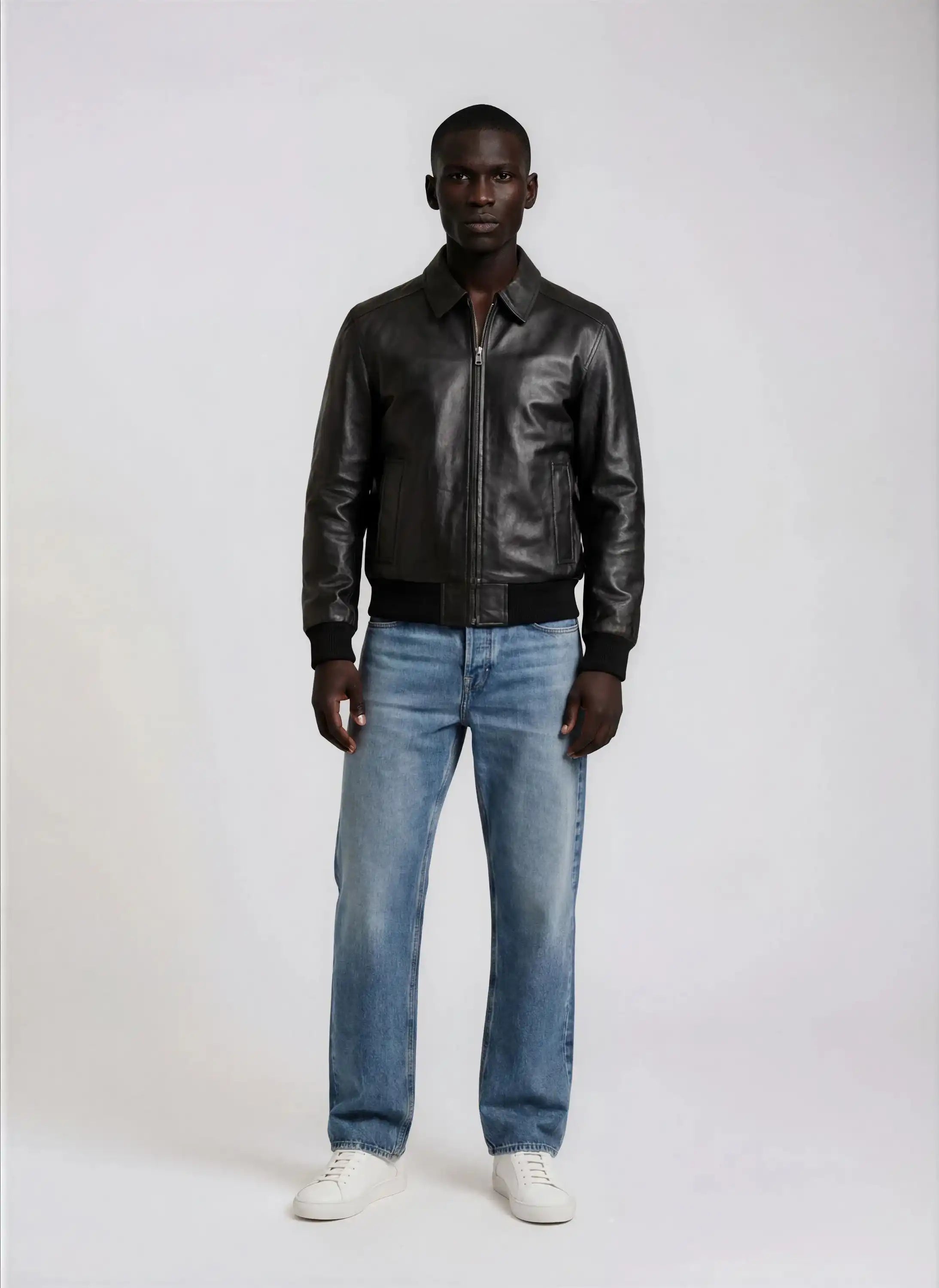 Ein Mann schaut nach vorne und trägt die trueprodigy Herren Lederjacke aus Schafsleder in Schwarz mit klassischem Blouson-Schnitt, hellblaue Jeans und weiße Turnschuhe vor einem schlichten hellen Hintergrund.