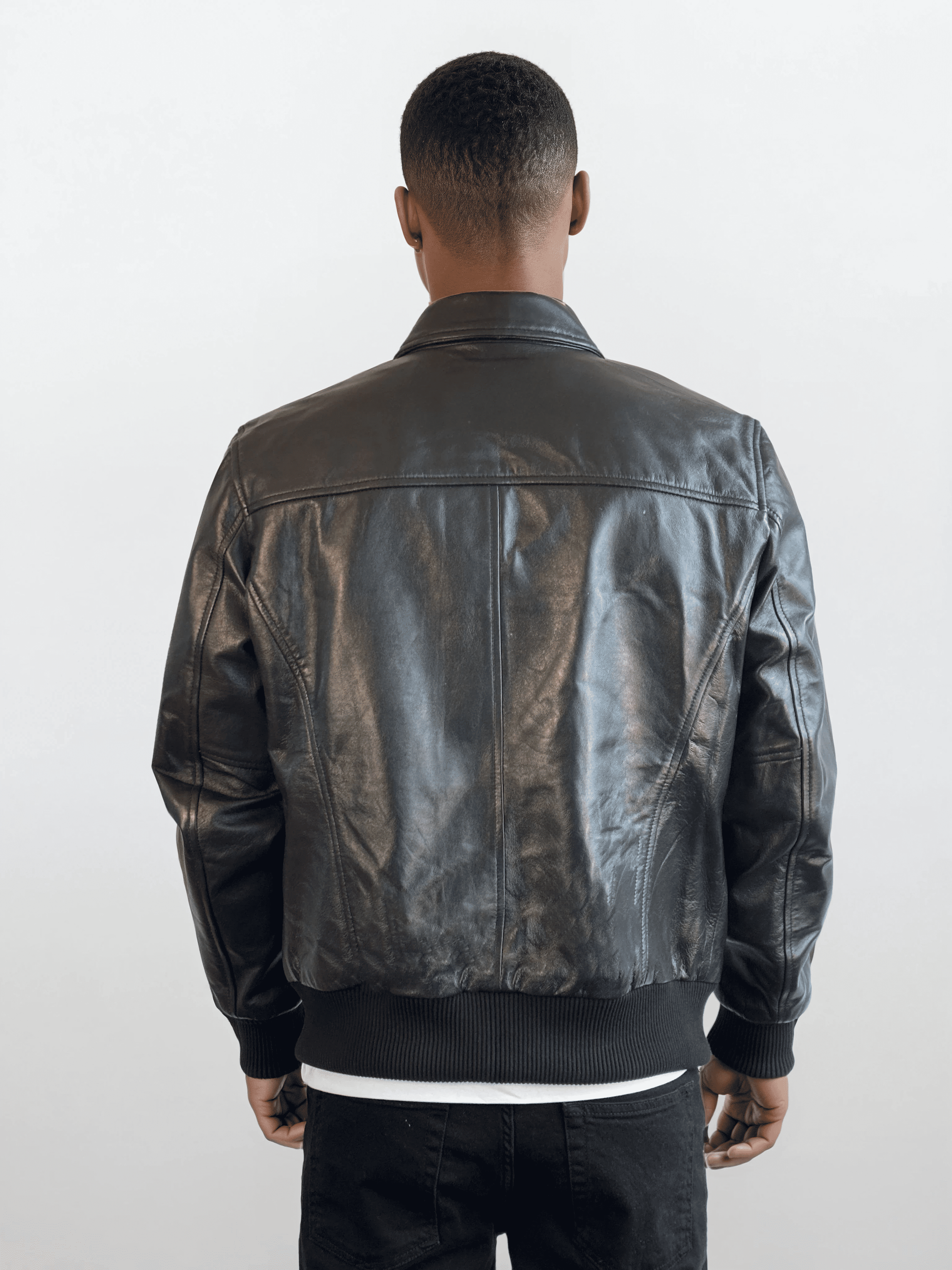 Eine Person mit kurzem Haar trägt die trueprodigy Herren Lederjacke aus Schafsleder in Schwarz im klassischen Blouson-Schnitt, dazu schwarze Hose und weißes Shirt. Der Hintergrund ist schlicht und hell.