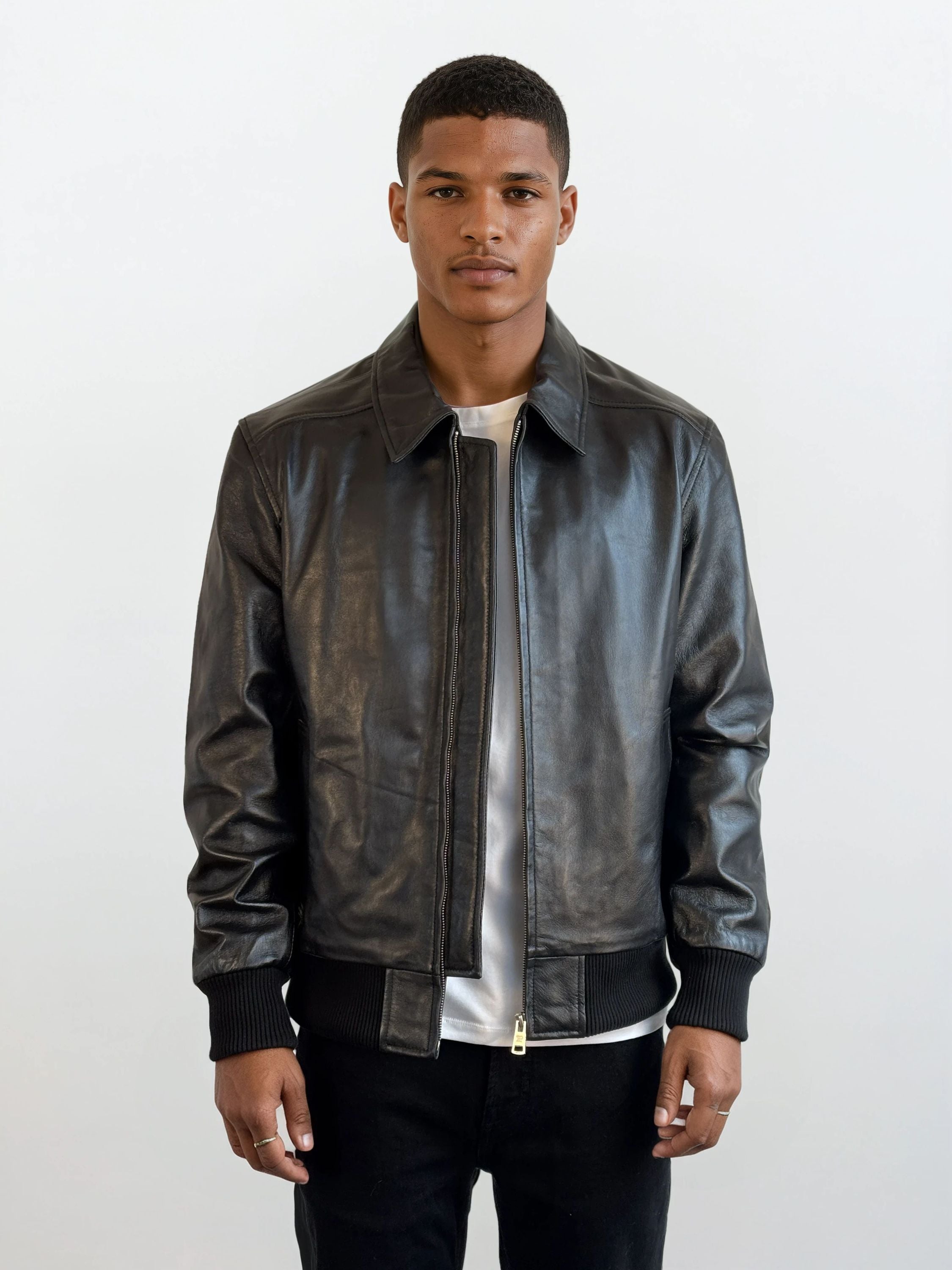 Ein Mann trägt die Herren Lederjacke aus Schafsleder in Schwarz mit klassischem Blouson-Schnitt von trueprodigy über einem weißen Shirt und schwarzen Hosen, steht entspannt vor hellem Hintergrund, die Hände an den Seiten.
