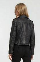 Eine Person mit langem, glattem blondem Haar wird von hinten gezeigt und trägt eine schwarze Bikerlederjacke Vintage Optik von trueprodigy und eine schwarze Jeans vor einem schlichten, hellen Hintergrund.