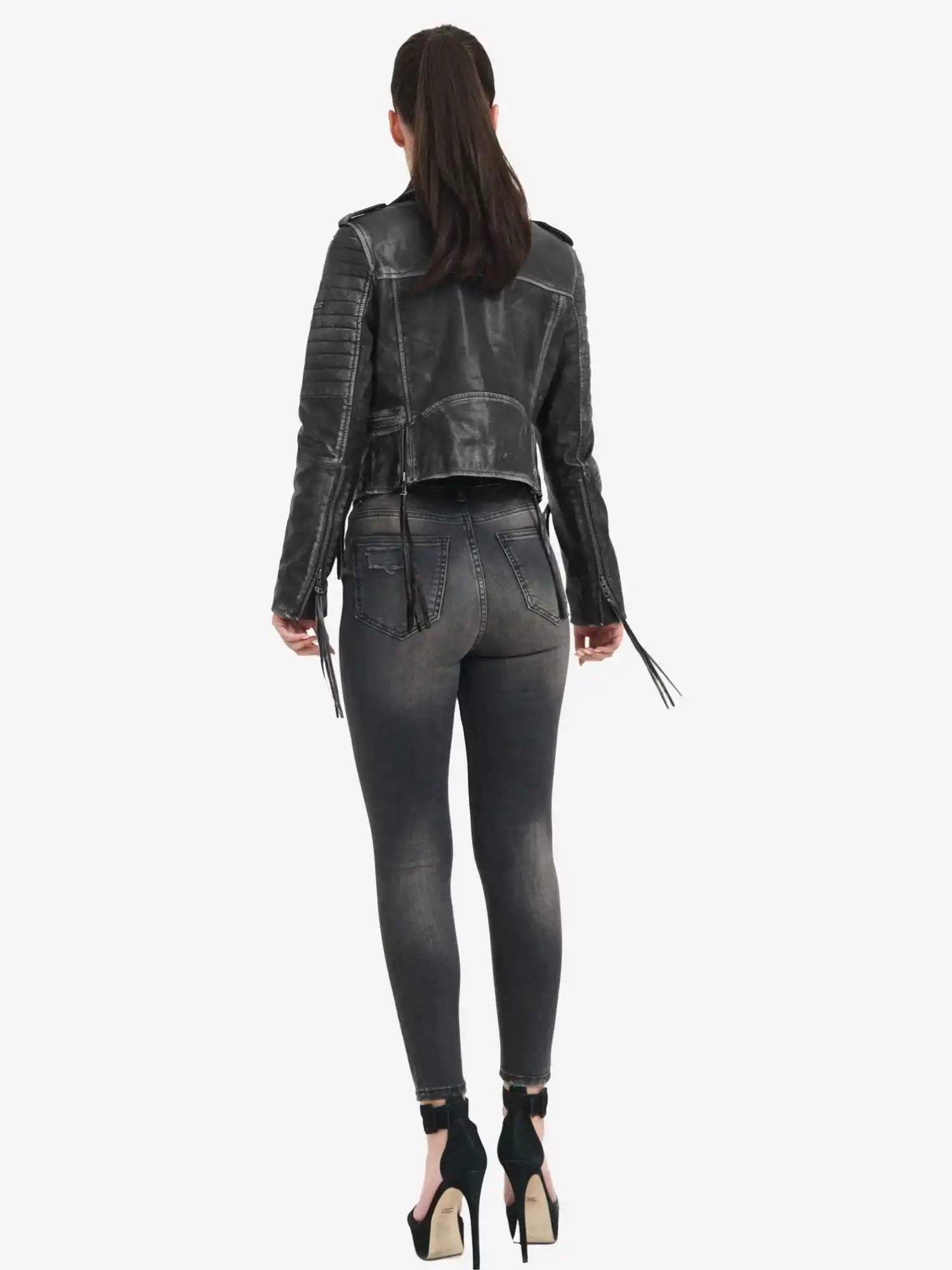 Eine Frau mit langen dunklen Haaren in einem Pferdeschwanz steht mit dem Rücken zur Kamera. Sie trägt die trueprodigy Avril Bikerlederjacke Vintage Optik, verwaschene schwarze Skinny Jeans und stylische schwarze hochhackige Schuhe.