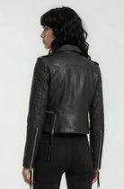 Eine Person mit gewellten dunklen Haaren ist von hinten zu sehen. Sie trägt die trueprodigy Biker Lederjacke und eine schwarze Hose und steht vor einem schlichten hellen Hintergrund.