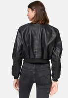 Eine Person mit glattem braunem Haar ist von hinten zu sehen. Sie trägt die trueprodigy Paola Kurze Oversized Lederjacke und eine schwarze Jeans mit hoher Taille vor einem schlichten weißen Hintergrund.