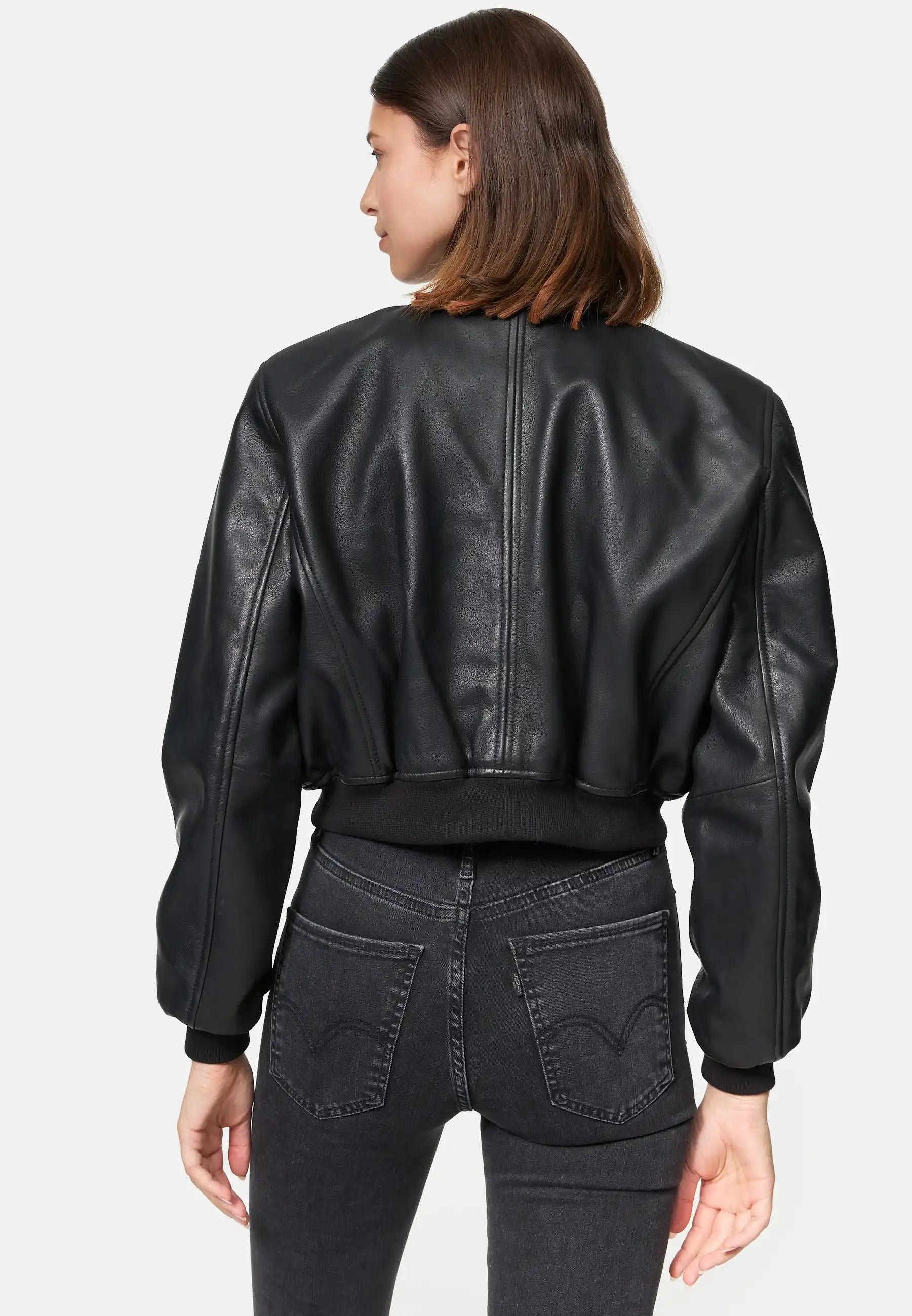 Eine Person mit glattem braunem Haar ist von hinten zu sehen. Sie trägt die trueprodigy Paola Kurze Oversized Lederjacke und eine schwarze Jeans mit hoher Taille vor einem schlichten weißen Hintergrund.