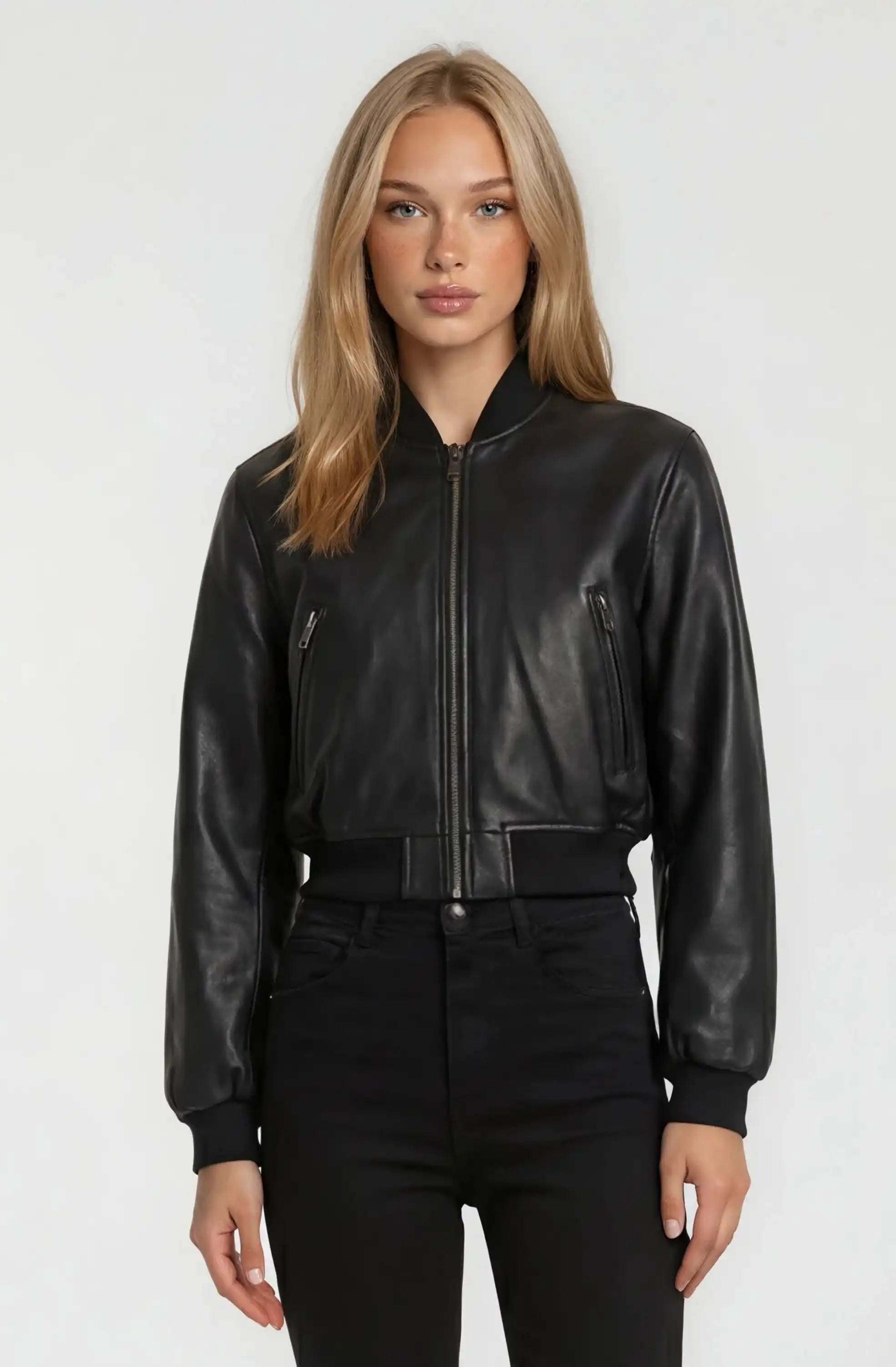 Eine Person mit langen blonden Haaren blickt nach vorne und trägt eine trueprodigy Kurze Oversized Lederjacke und eine schwarze Hose vor einem schlichten hellen Hintergrund.