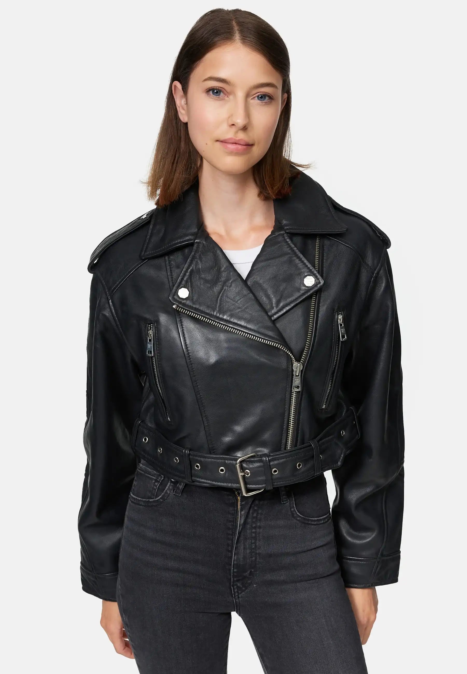 Eine Frau mit glattem braunem Haar trägt eine Trueprodigy Rosa Kurze Bomber-Lederjacke über einem weißen Oberteil und einer schwarzen Jeans mit hoher Taille. Sie steht vor einem schlichten hellen Hintergrund.