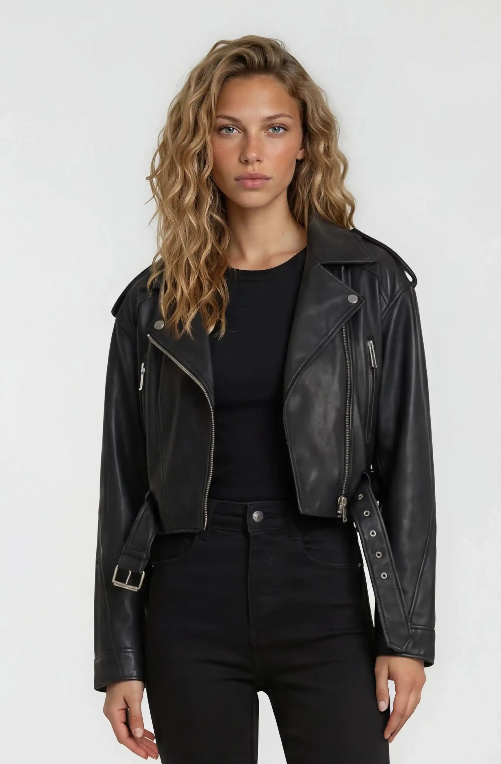 Eine Person mit gewelltem blondem Haar trägt eine trueprodigy Kurze Bomber-Lederjacke über einem schwarzen Hemd und einer schwarzen Hose und steht vor einem schlichten hellen Hintergrund.