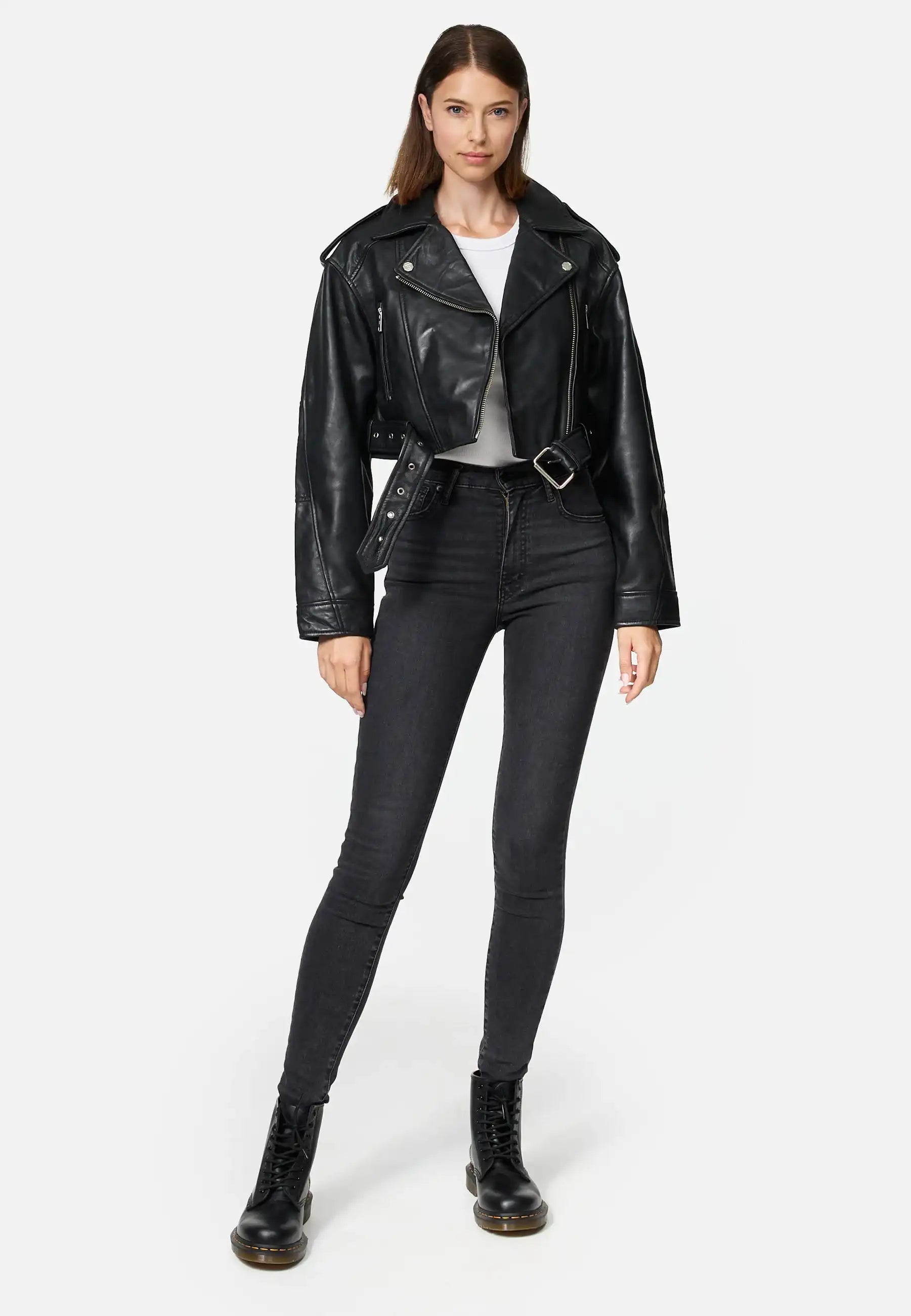 Eine Frau mit glattem, schulterlangem braunem Haar posiert vor einem unifarbenen Hintergrund und trägt eine Rosa Kurze Bomber-Lederjacke von trueprodigy, ein weißes T-Shirt, schwarze Skinny Jeans mit hoher Taille und schwarze Schnürstiefel.