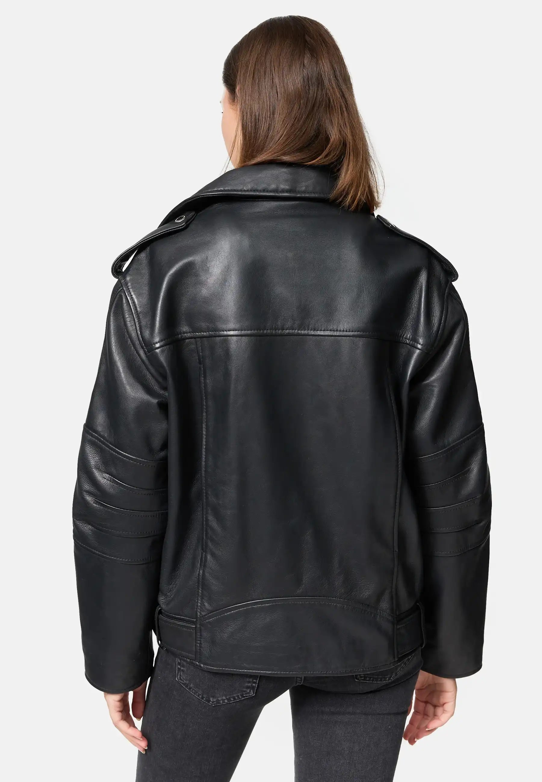 Eine Person mit glattem braunem Haar wird von hinten gezeigt, die eine Trueprodigy Dua Lange übergroße Bikerlederjacke mit breiten Schultern und dunkelgraue Jeans vor einem schlichten hellen Hintergrund trägt.