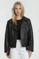 Eine Frau mit langen blonden Haaren trägt eine Lange übergroße Bikerlederjacke von trueprodigy aus weichem Schafsleder, steht vor einem schlichten hellen Hintergrund und schaut mit neutralem Blick direkt in die Kamera.