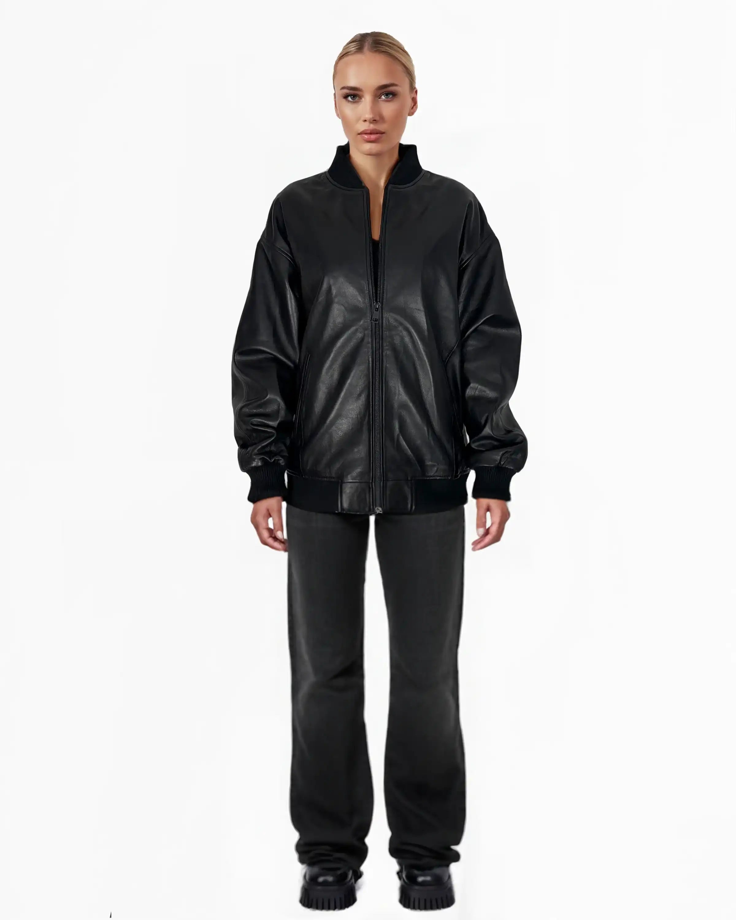Eine Person steht mit Blick nach vorne in einer Trueprodigy Selina Oversize-Bomberjacke aus Leder mit Rippbündchen & schwarzem Reißverschluss, schwarzer Hose und schwarzen Schuhen vor einem schlichten weißen Hintergrund.