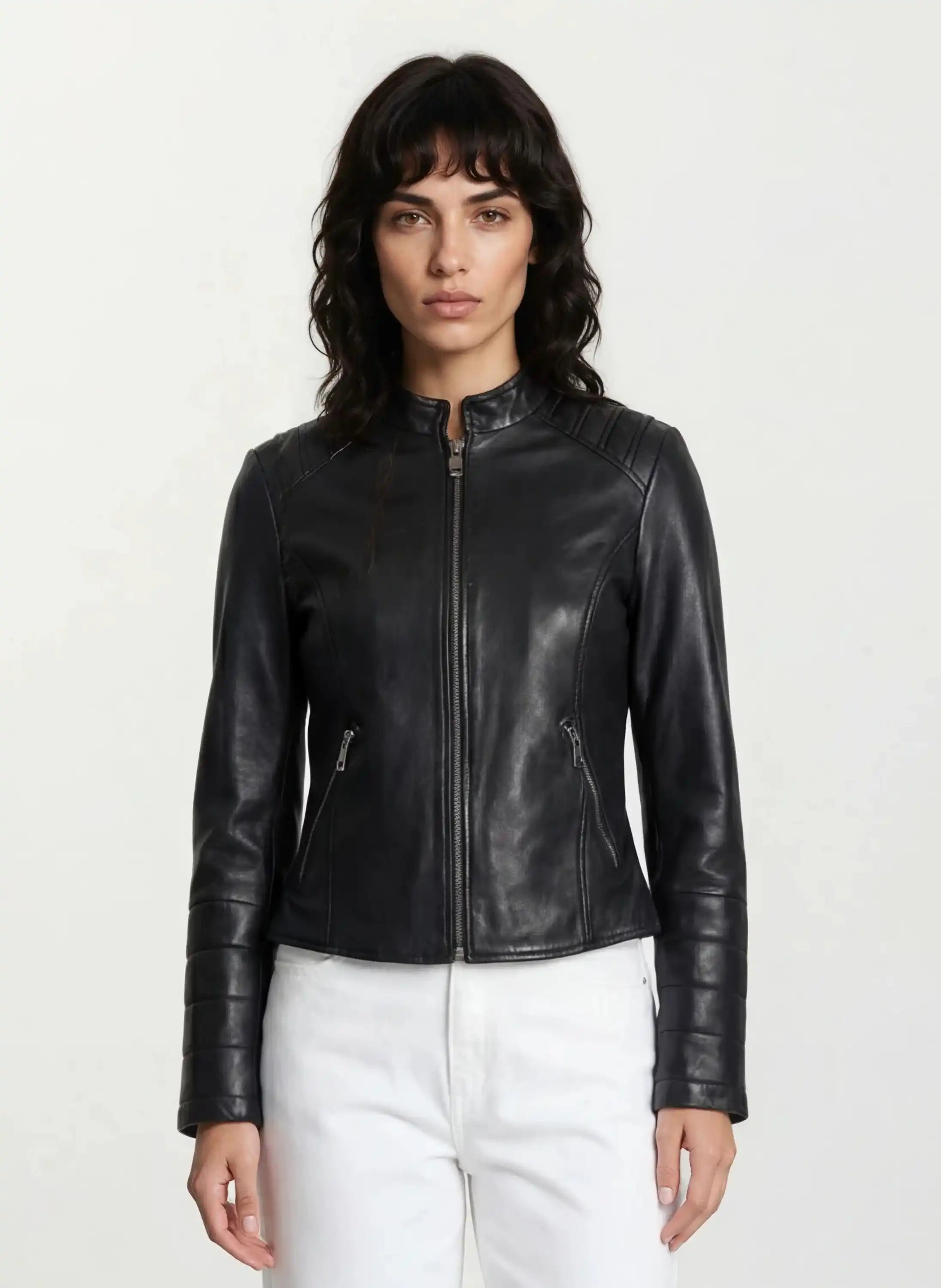 Eine Person mit langen, gewellten dunklen Haaren trägt die taillierte trueprodigy Lederjacke mit Stehkragen, Steppnähten & silbernen Reißverschlüssen und weißen Hosen, steht vor hellem Hintergrund und blickt neutral in die Kamera für einen rockigen Look.