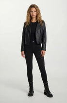 Eine Frau mit langem, gewelltem Haar steht mit dem Gesicht nach vorne und trägt eine taillierte trueprodigy Lederjacke mit schwarzem Reißverschluss & Ärmelzipper, schwarzem Shirt, Skinny Jeans und Schnürboots vor hellem Hintergrund.