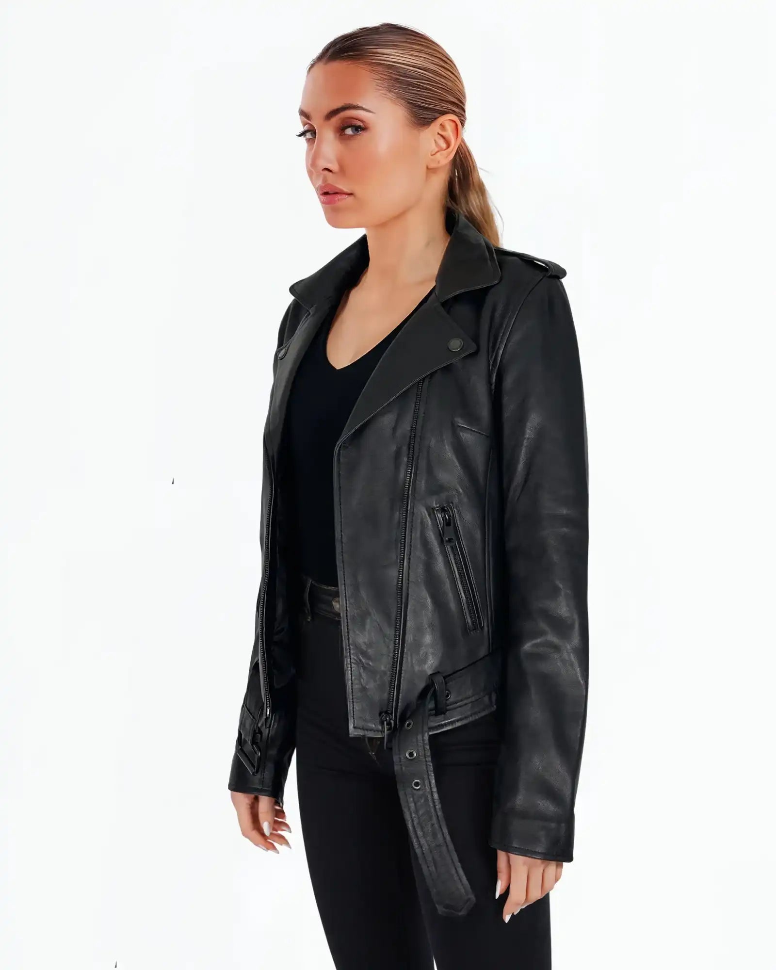 Eine Frau steht vor einem weißen Hintergrund und trägt die trueprodigy Laura Feminine Bikerjacke mit Gürtel & Schulterriegeln über einem schwarzen Oberteil und einer schwarzen Hose. Sie hat ihr Haar zurückgebunden und schaut leicht zur Seite.