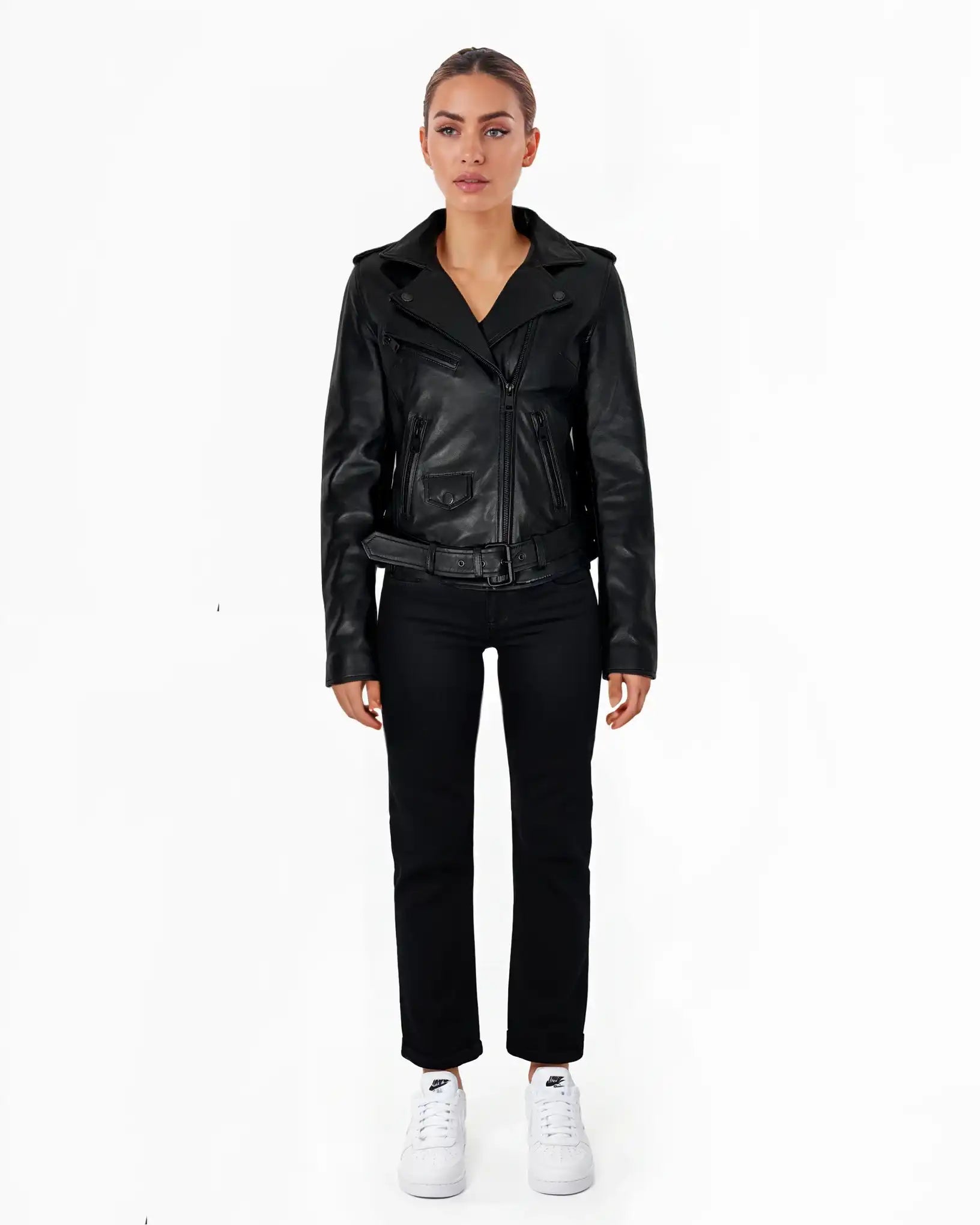 Eine Frau steht mit dem Gesicht nach vorne vor einem weißen Hintergrund und trägt die trueprodigy Laura Feminine Bikerjacke mit Gürtel & Schulterriegeln, eine schwarze Hose und weiße Turnschuhe. Ihre Arme ruhen an ihren Seiten und sie hat einen neutralen Gesichtsausdruck.