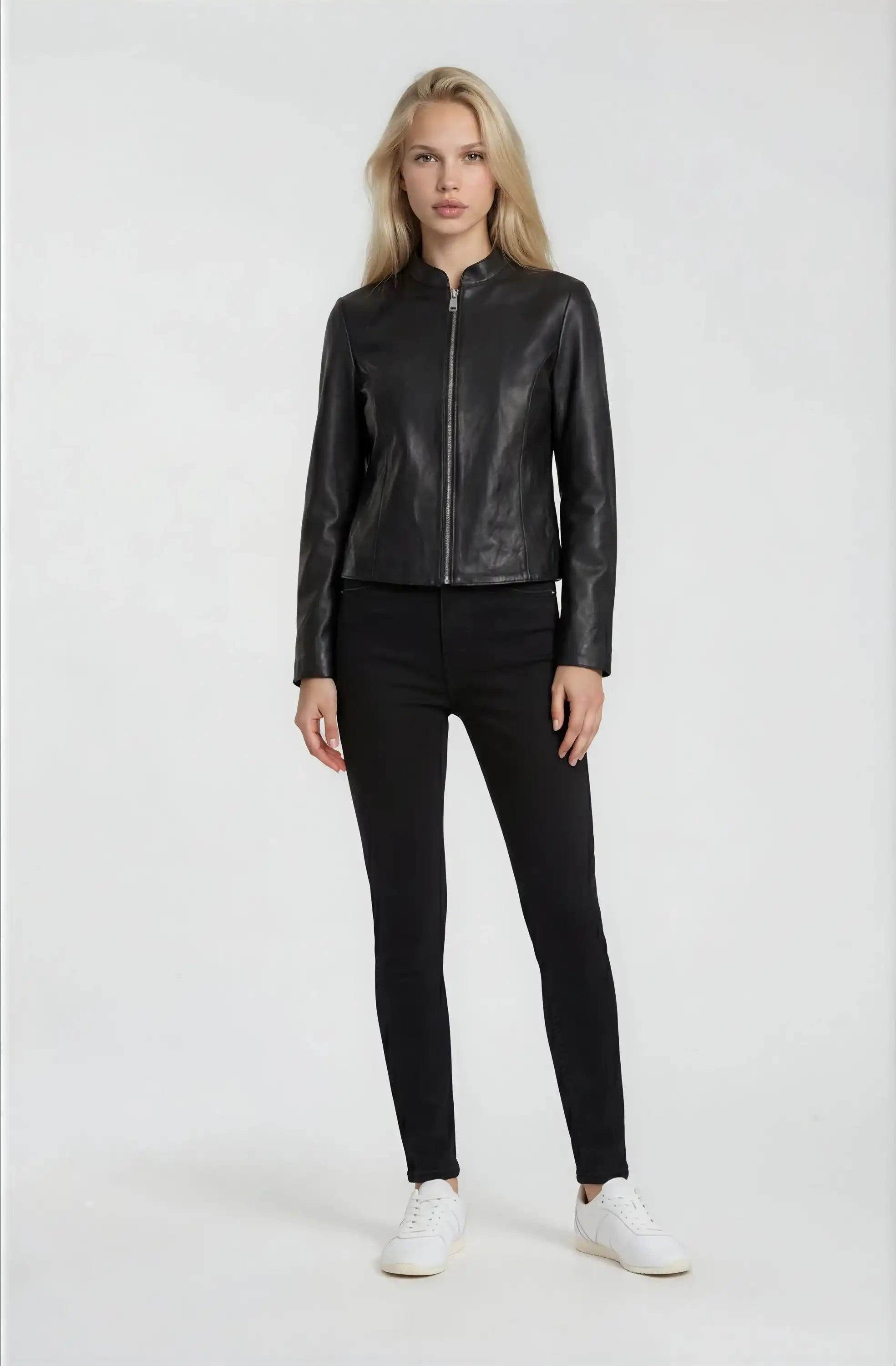 Eine Frau trägt die trueprodigy Damen Lederjacke aus Schafsleder in Schwarz mit minimalistischem Design, dazu schwarze Hose und weiße Sneaker. Sie hat lange blonde Haare und steht vor weißem Hintergrund.