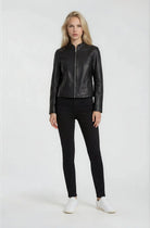 Eine Frau trägt die trueprodigy Damen Lederjacke aus Schafsleder in Schwarz mit minimalistischem Design, dazu schwarze Hose und weiße Sneaker. Sie hat lange blonde Haare und steht vor weißem Hintergrund.