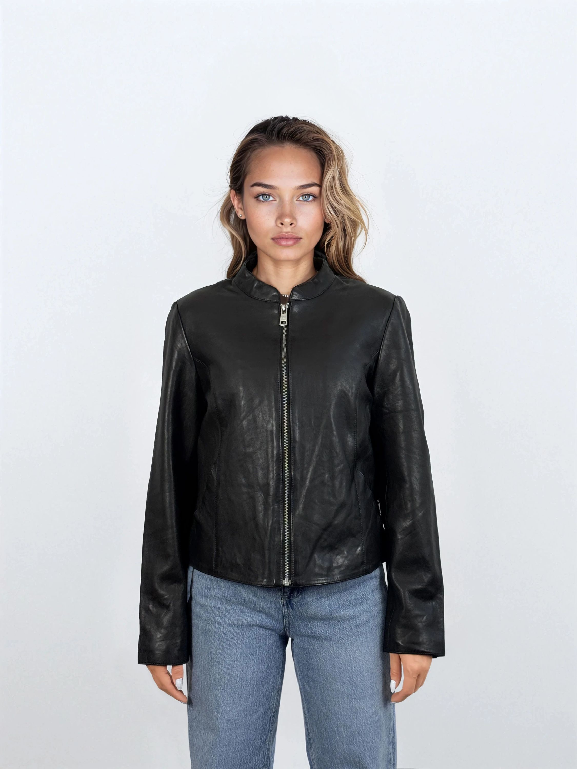 Eine Person mit hellbraunem Haar, die die trueprodigy Damen Lederjacke aus Schafsleder in Schwarz mit minimalistischem Design und Blue Jeans trägt, steht mit dem Gesicht nach vorne vor einem schlichten weißen Hintergrund.