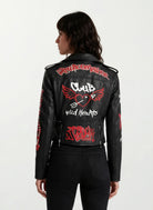 Eine Frau mit mittellangen dunklen Haaren ist von hinten zu sehen. Sie trägt die trueprodigy Feminine Lederjacke mit Grafittiprint und Reißverschluss, eine schwarze Lederjacke mit roten und weißen Graffiti-Grafiken und Text.