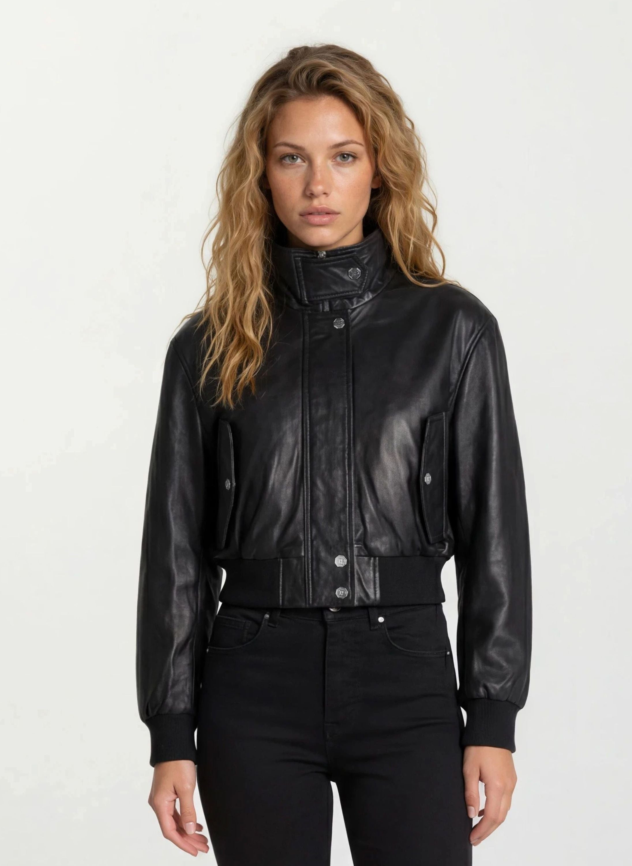 Eine Frau mit gewelltem, hellbraunem Haar trägt die trueprodigy Feminine Lederjacke Stehkragen und Reißverschluss und eine schwarze Hose und steht vor einem schlichten, hellen Hintergrund.